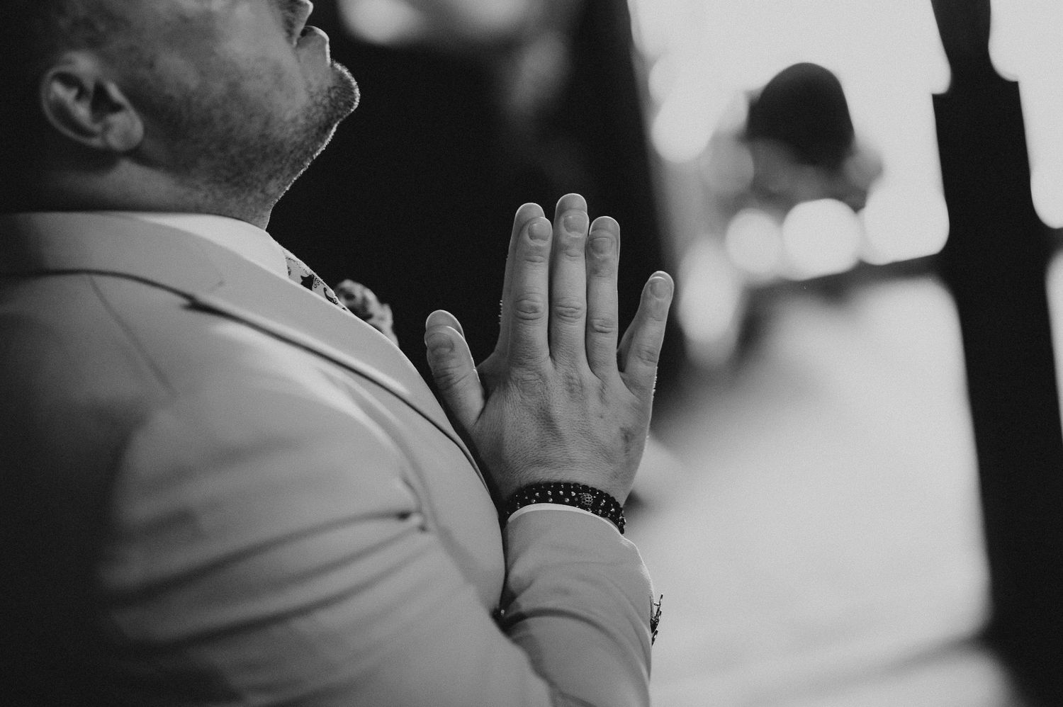 Close-up black and white photo of man with hands clasped in prayer at religious ceremony.