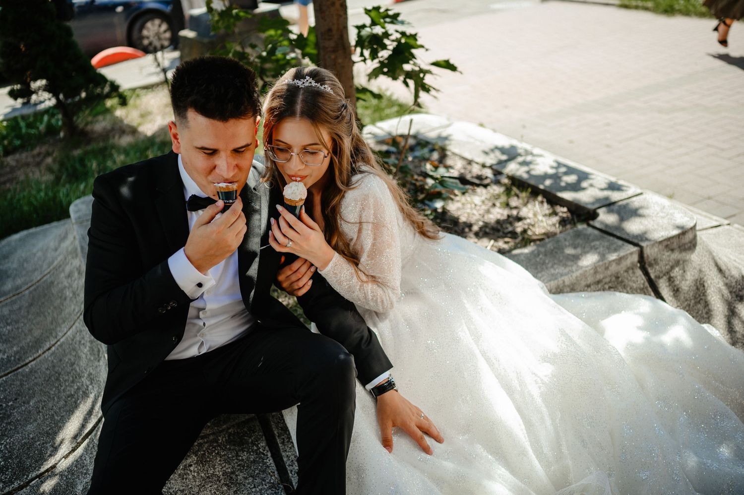 Bride and groom sitting together smelling a white flower on their wedding day outdoors.