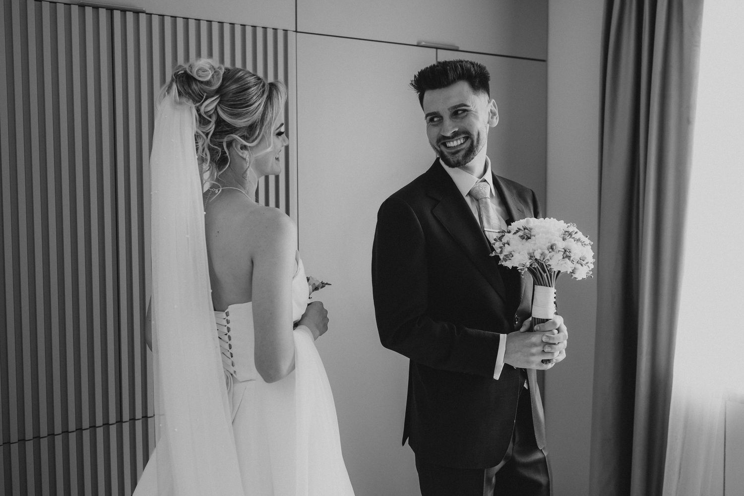 Groom smiling at bride in wedding dress during first look moment, black and white wedding photo.