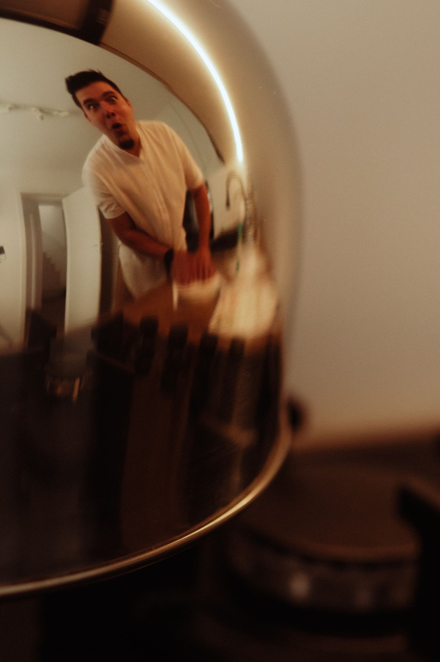 Creative reflection of a surprised man in white shirt captured in a shiny metallic kettle.