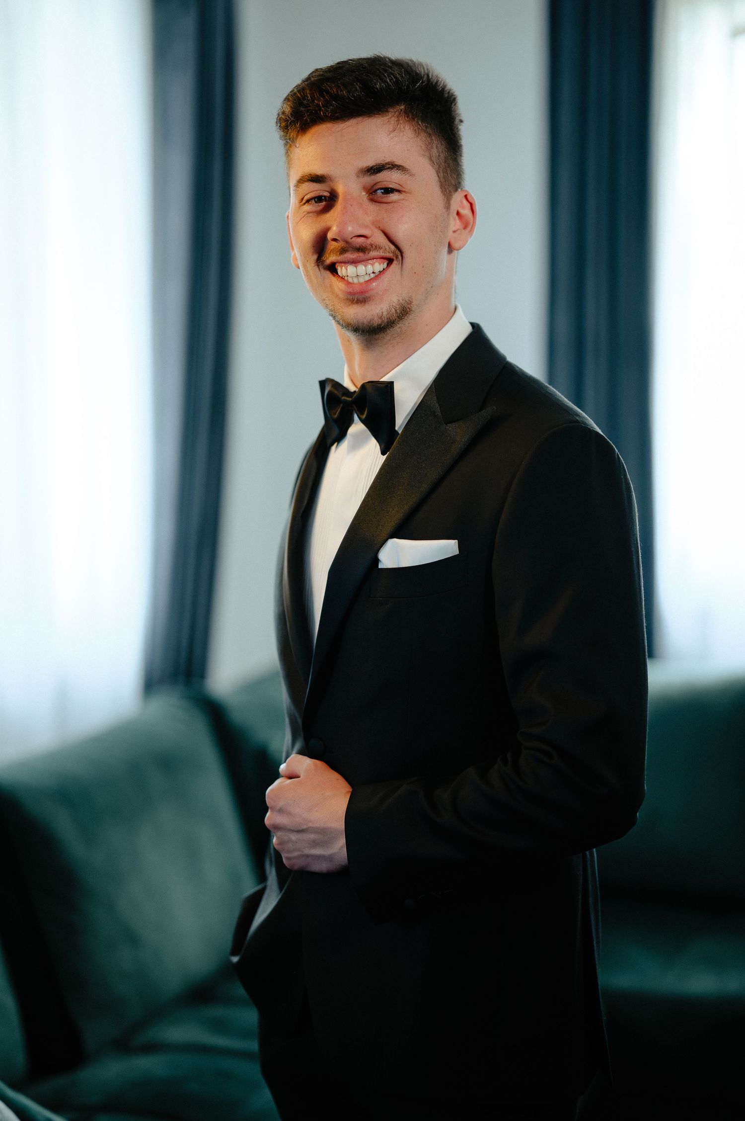 Smiling groom in black tuxedo with bow tie and white pocket square.