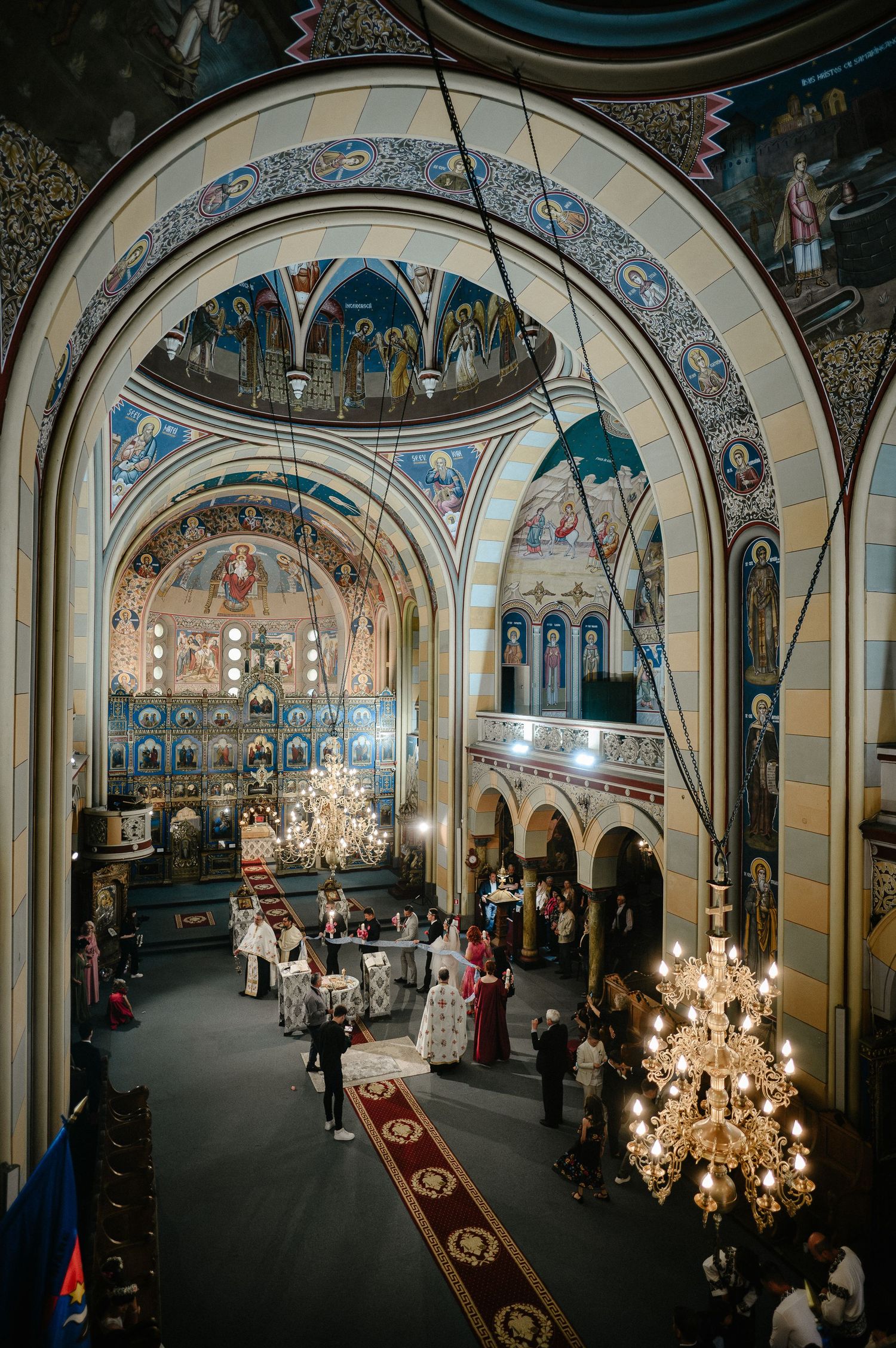 Grand Orthodox church interior with arched ceilings, Byzantine frescoes, and wedding ceremony below.