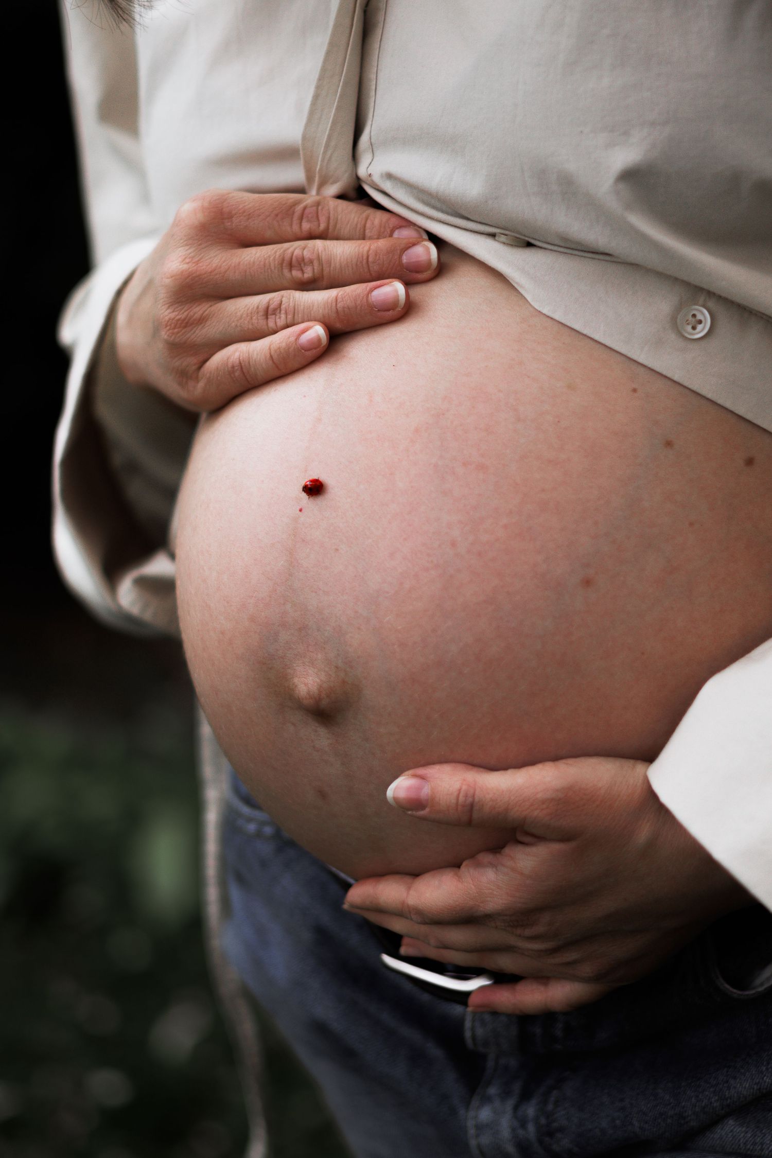 Close up of pregnant belly being held gently with both hands outdoors.