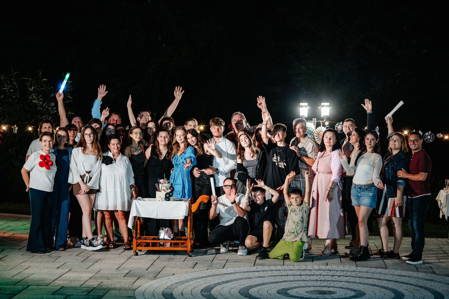 Large group of party guests posing and raising hands at an outdoor 18th birthday celebration.