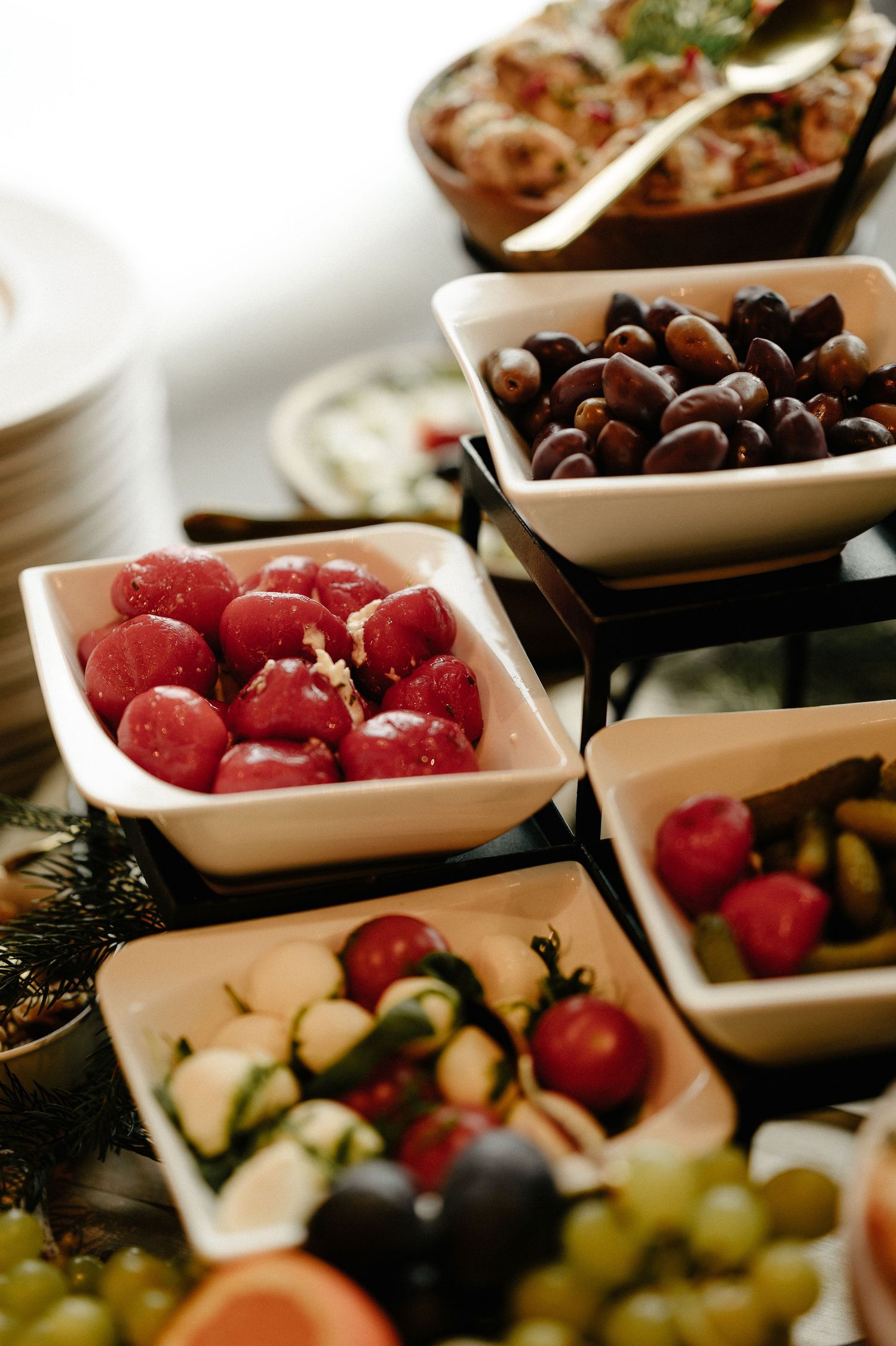 White ceramic bowls filled with marinated olives, cherry tomatoes, and pickled vegetables on a catering table.