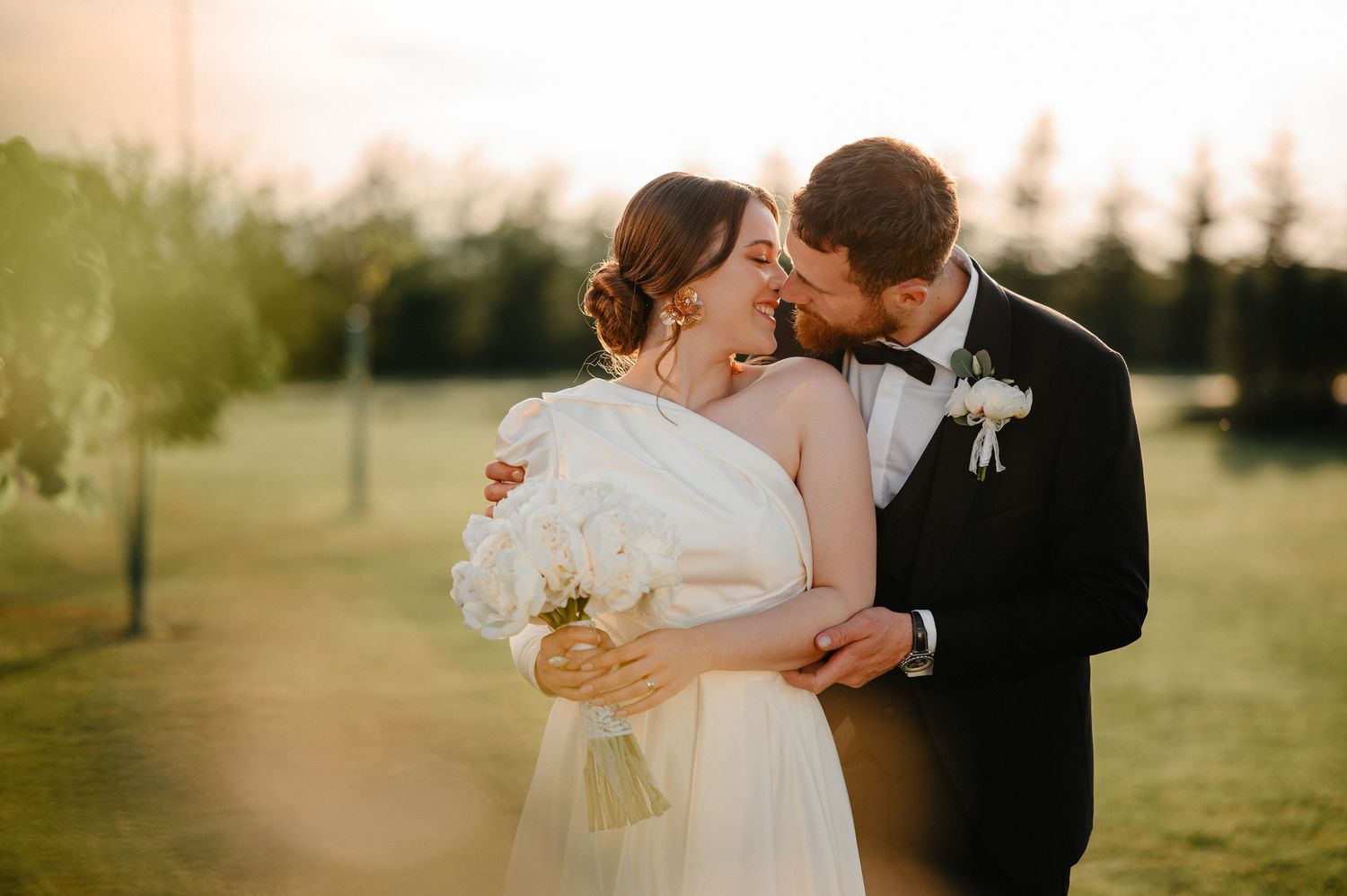 Groom kissing bride on cheek outdoors at golden sunset during wedding photography.