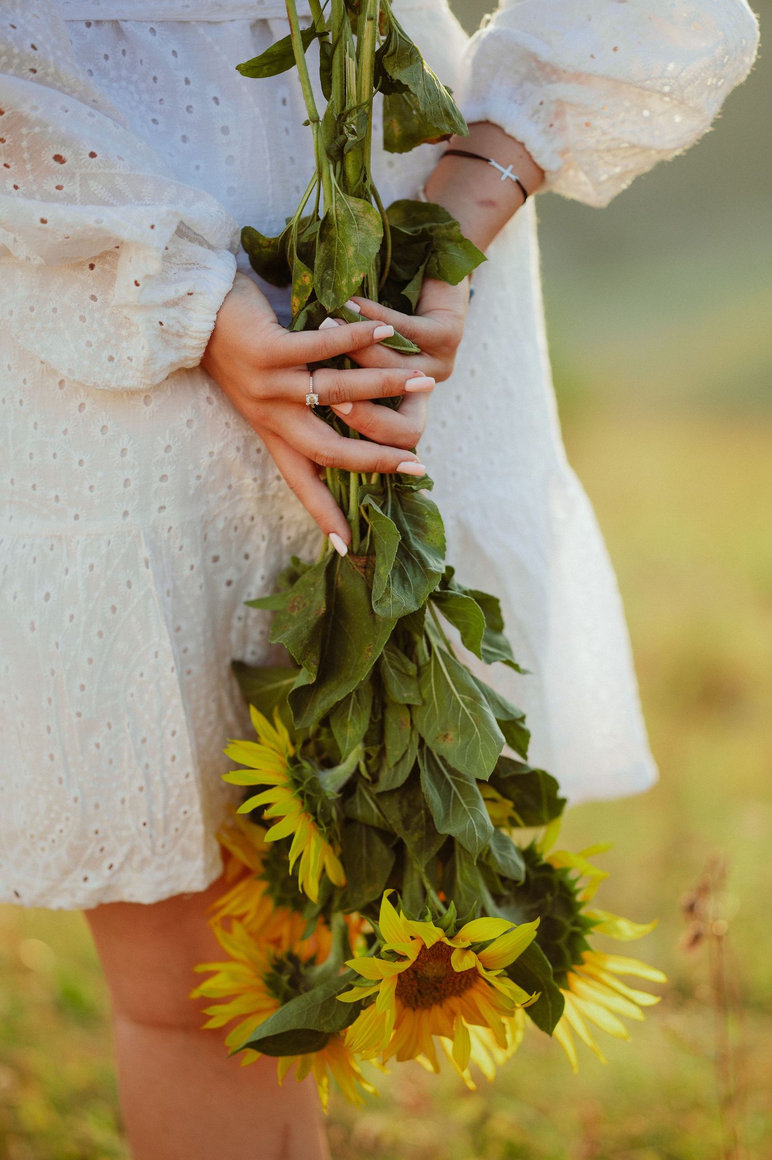 Close-up of woman in white lace dress holding sunflowers upside down in a sunny field.