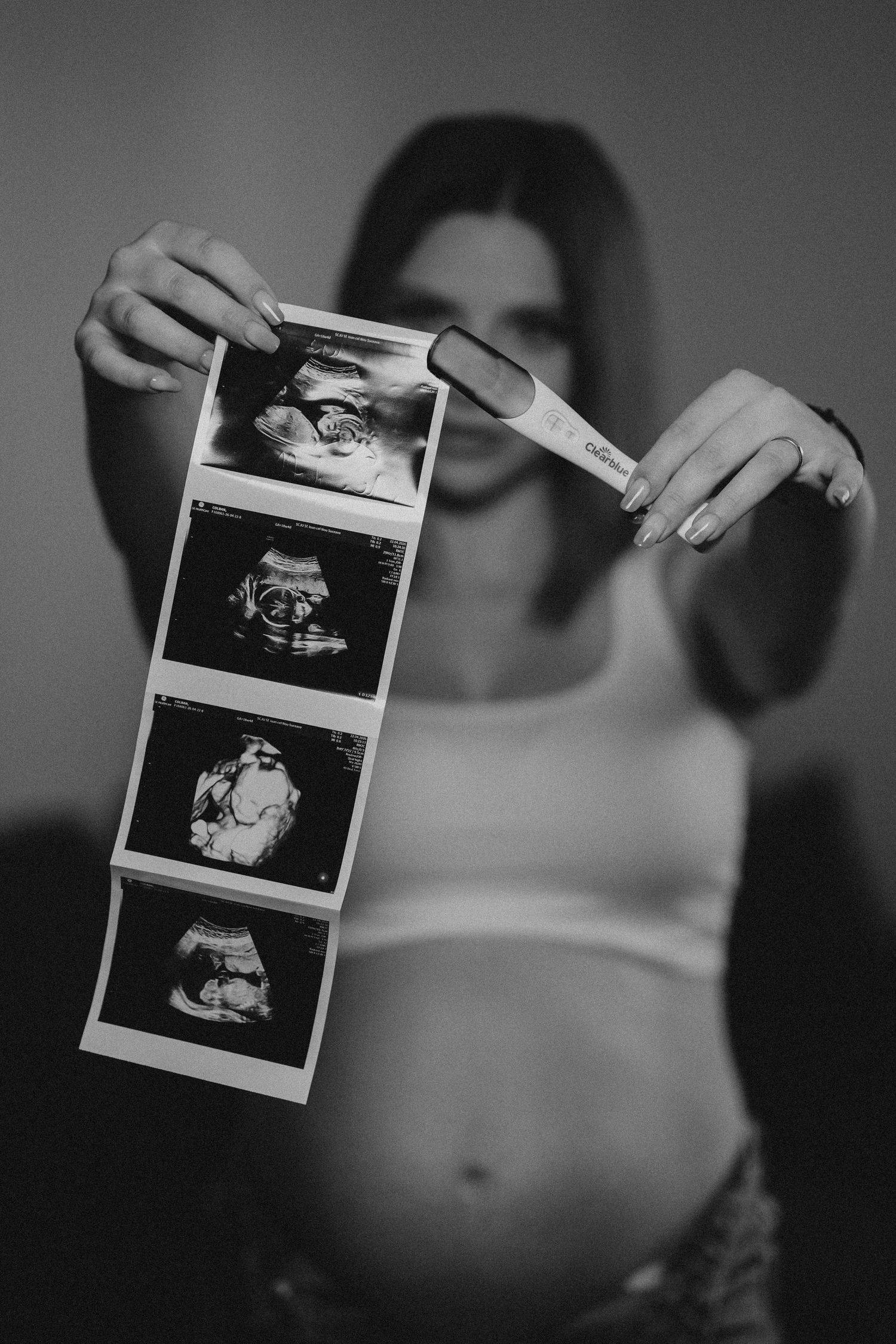 Pregnant woman holding ultrasound photos and pregnancy test in black and white maternity photo.