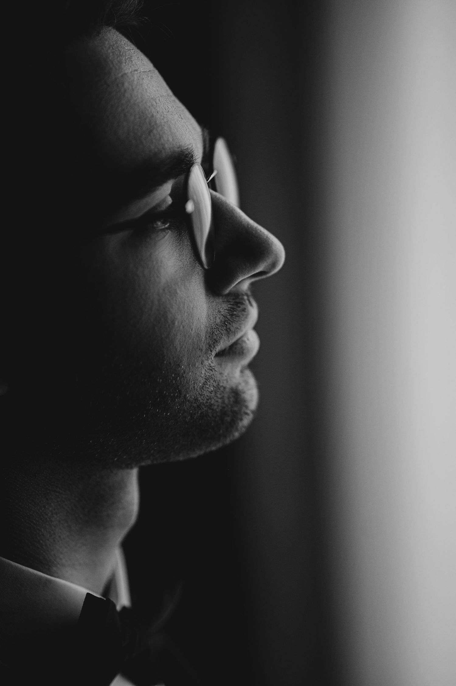 Black and white profile portrait of a man wearing glasses in dramatic side lighting.