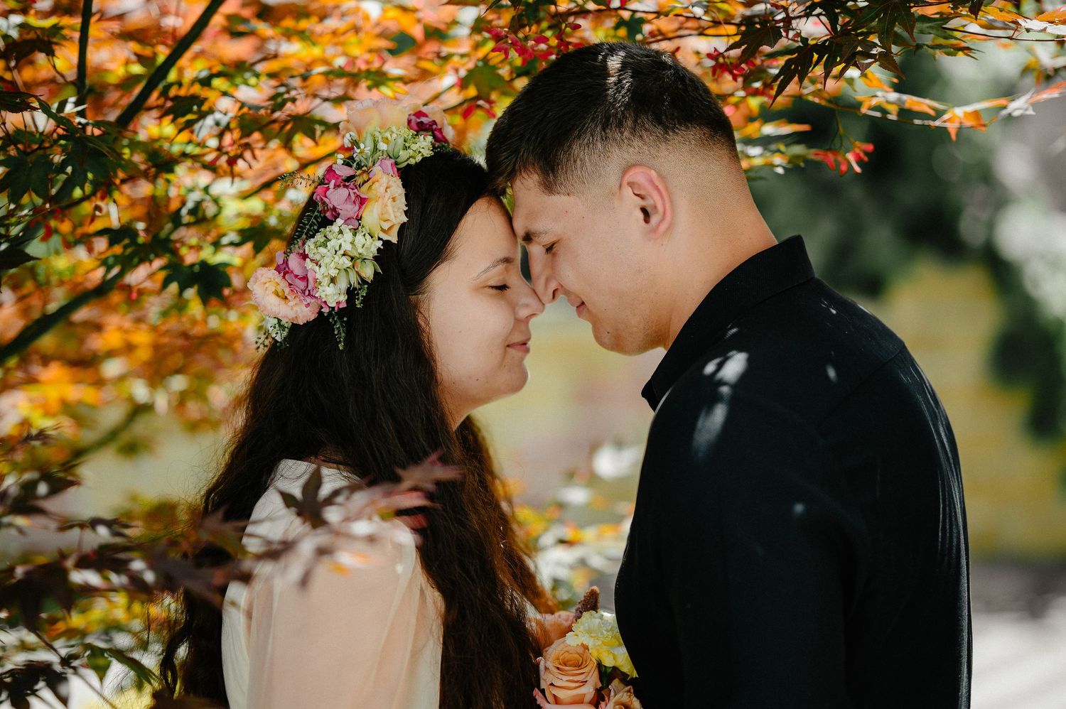 Couple sharing a romantic moment under colorful autumn foliage, woman wearing a floral crown.