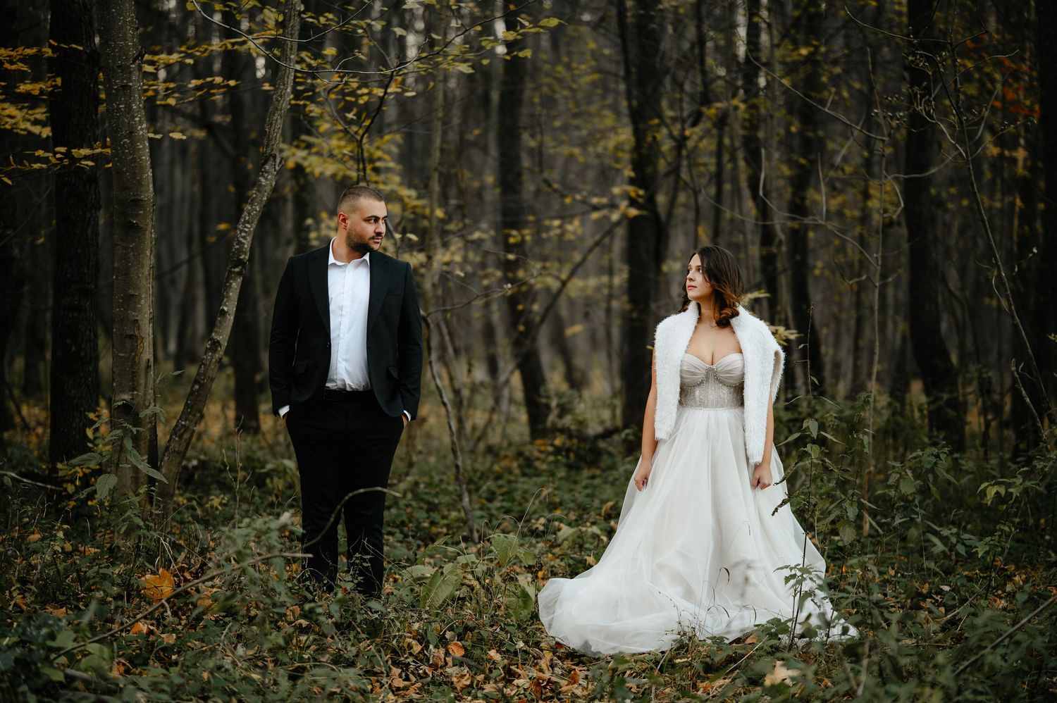 Bride and groom share a romantic moment in an autumn forest, with the bride in a flowing white gown.