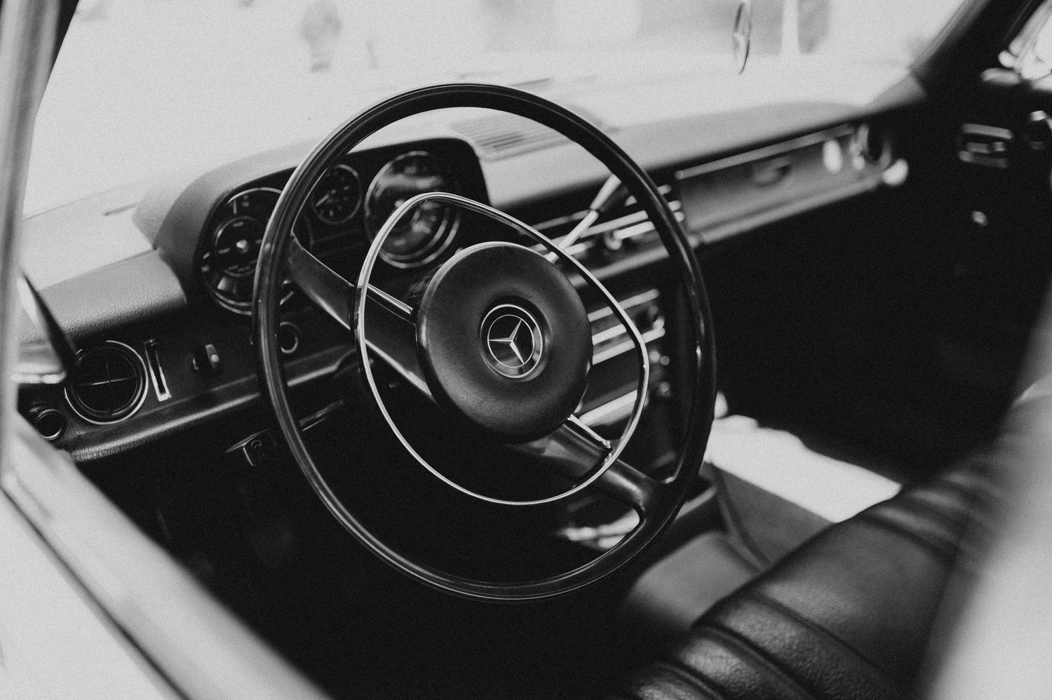 Classic Mercedes-Benz steering wheel and dashboard interior in elegant black and white photography.