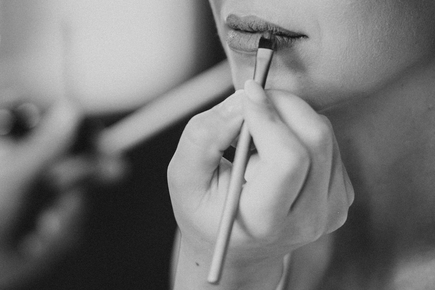 Close-up black and white photo of makeup artist applying lipstick to a bride.