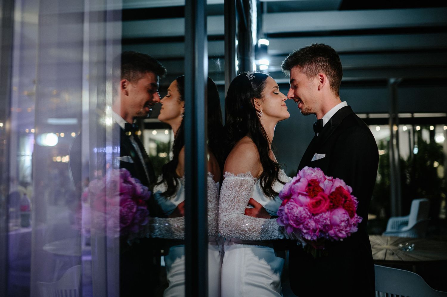 Romantic bride and groom sharing an intimate moment reflected in glass doors at Golden Forest venue.