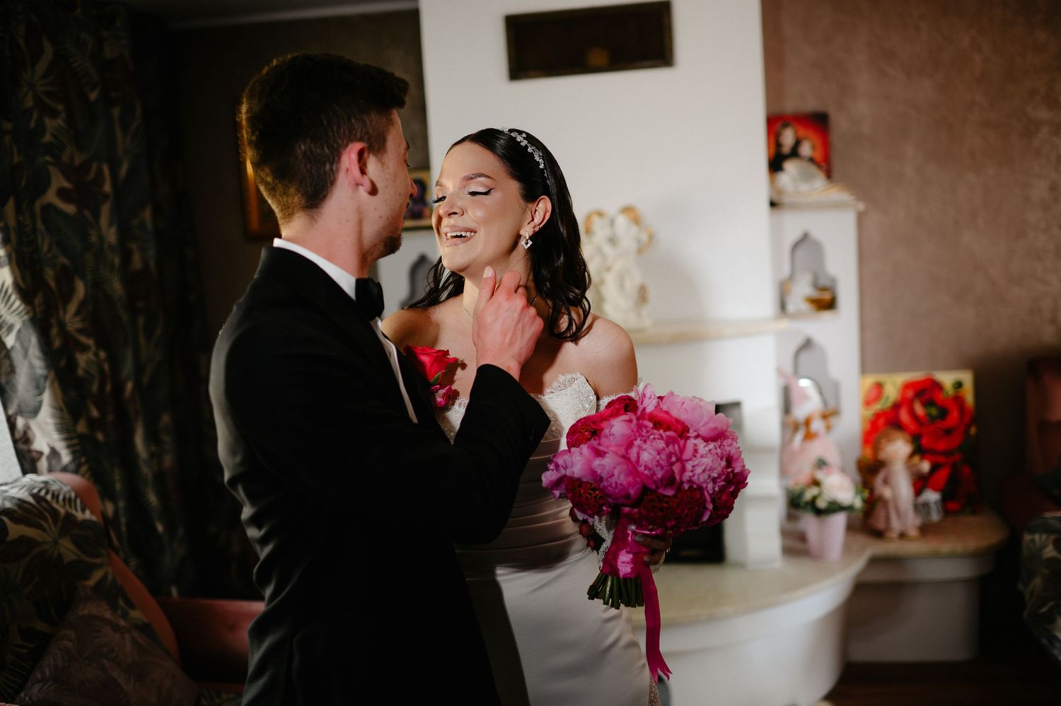 Bride smiles radiantly at groom who gently touches her face during intimate wedding moment indoors.