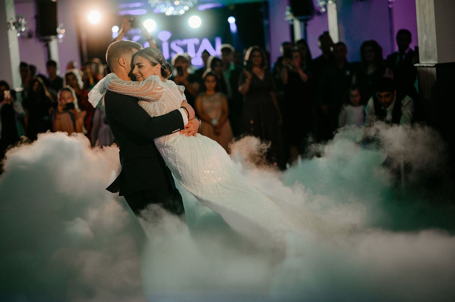 Newlyweds share first dance surrounded by romantic dry ice fog effect on wedding dance floor.