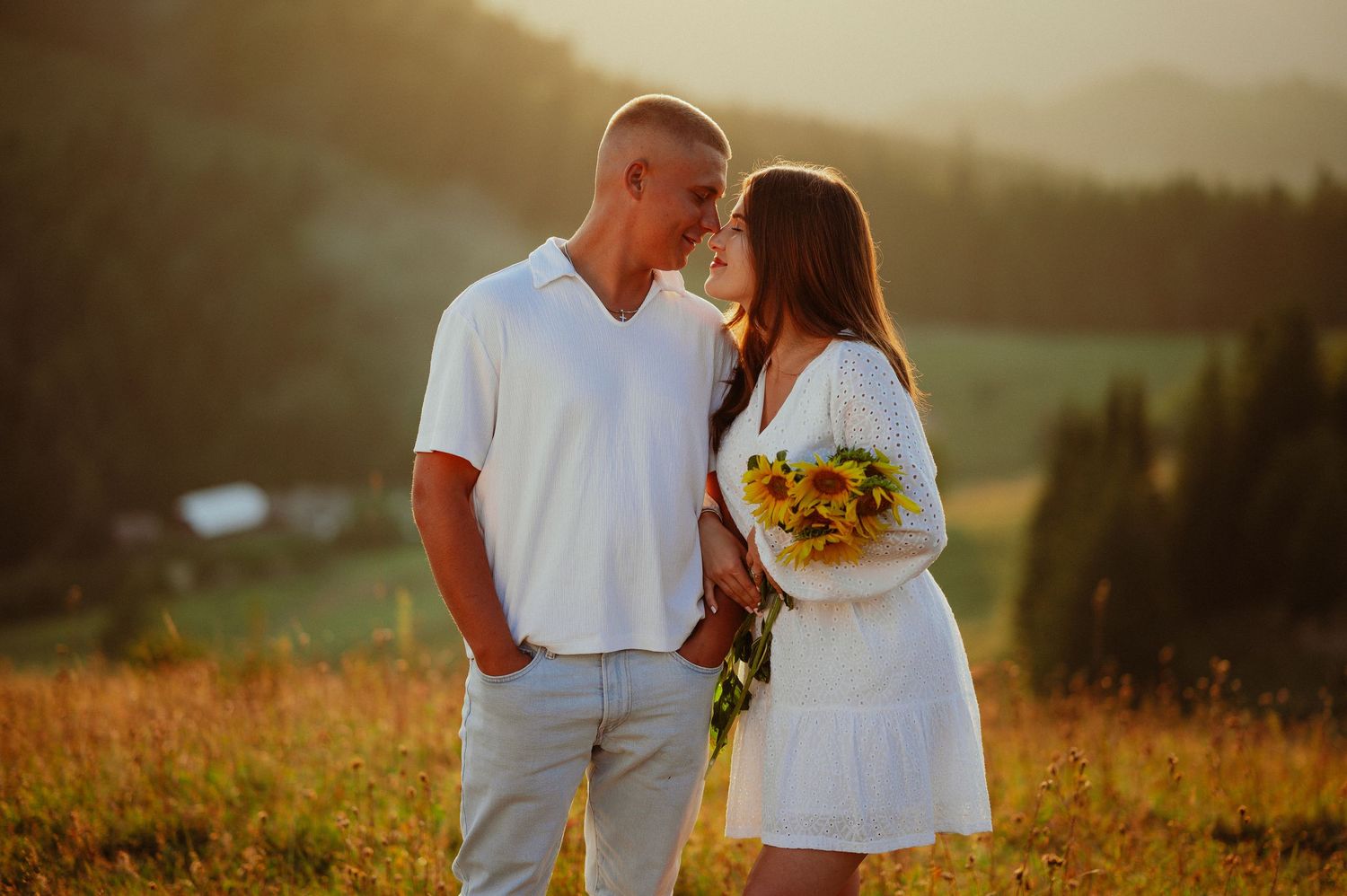 Young couple in white gazing at each other with sunflowers in a golden field.