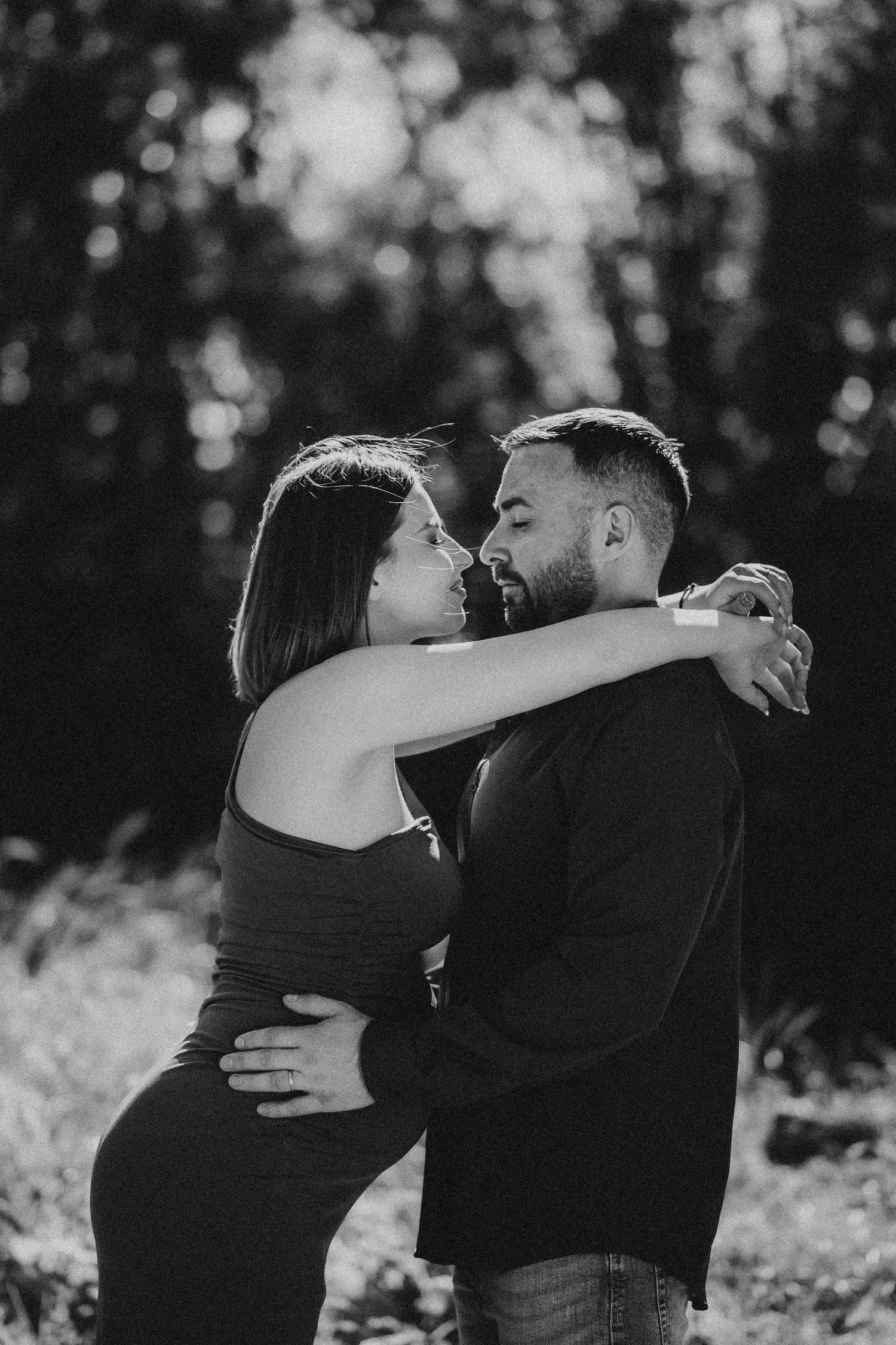 Black and white photo of a couple embracing tenderly in a forest setting.
