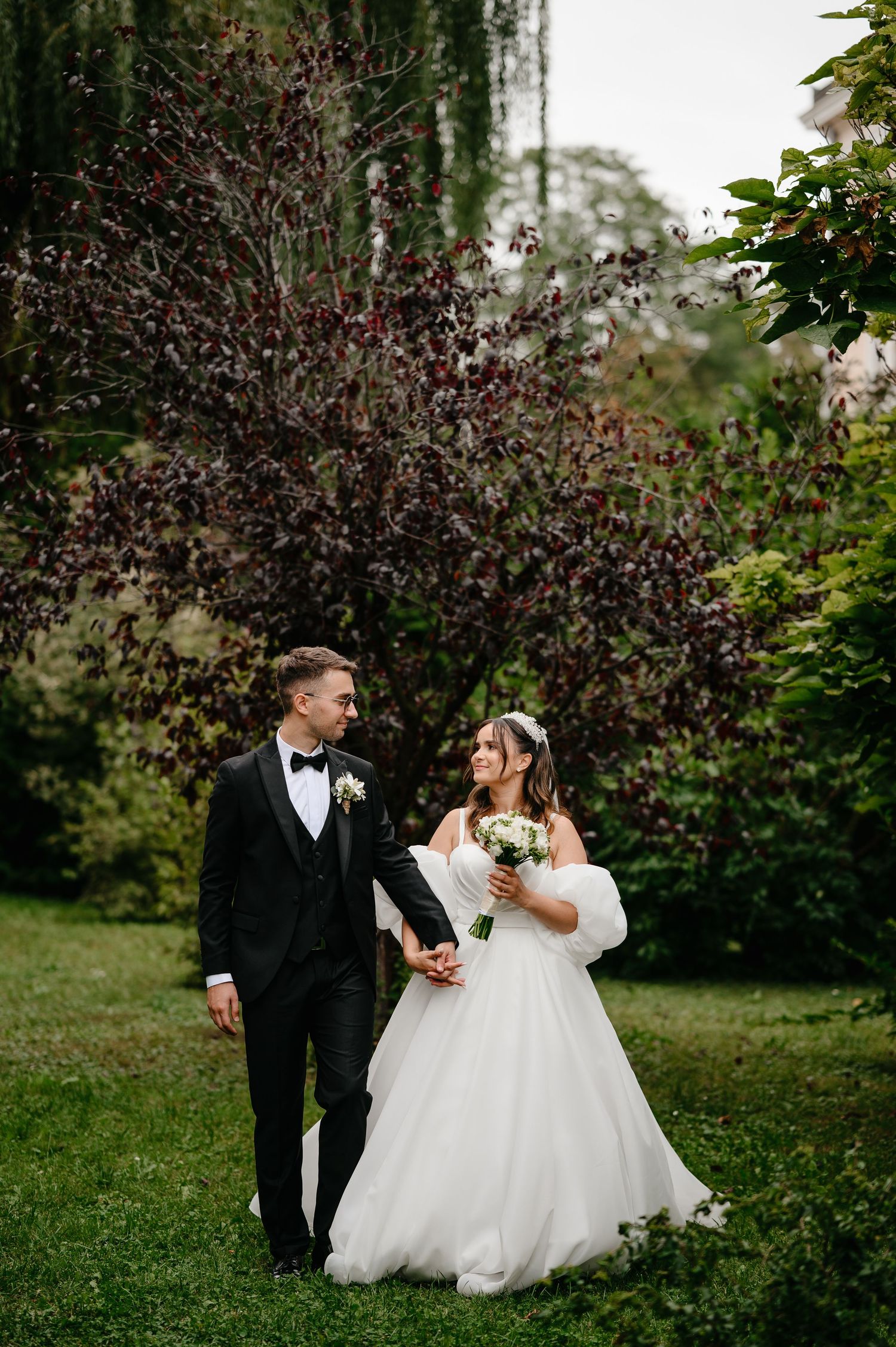 Bride and groom holding hands walking in lush garden on wedding day.