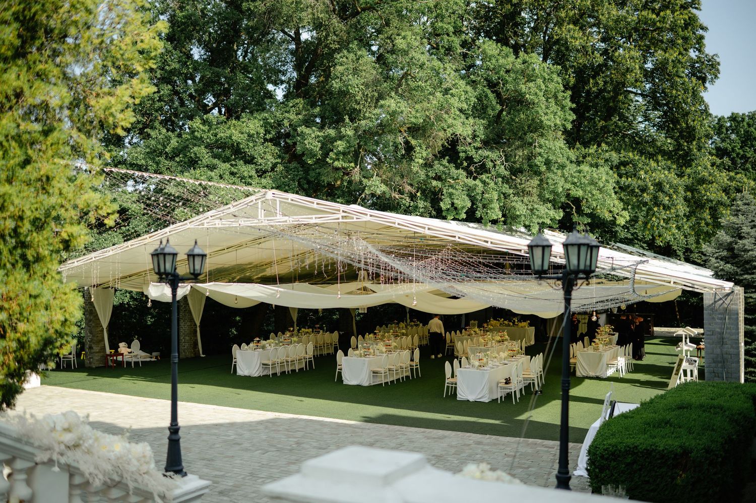 Grand outdoor wedding reception tent with black lanterns, white draping, and elegant table arrangements.