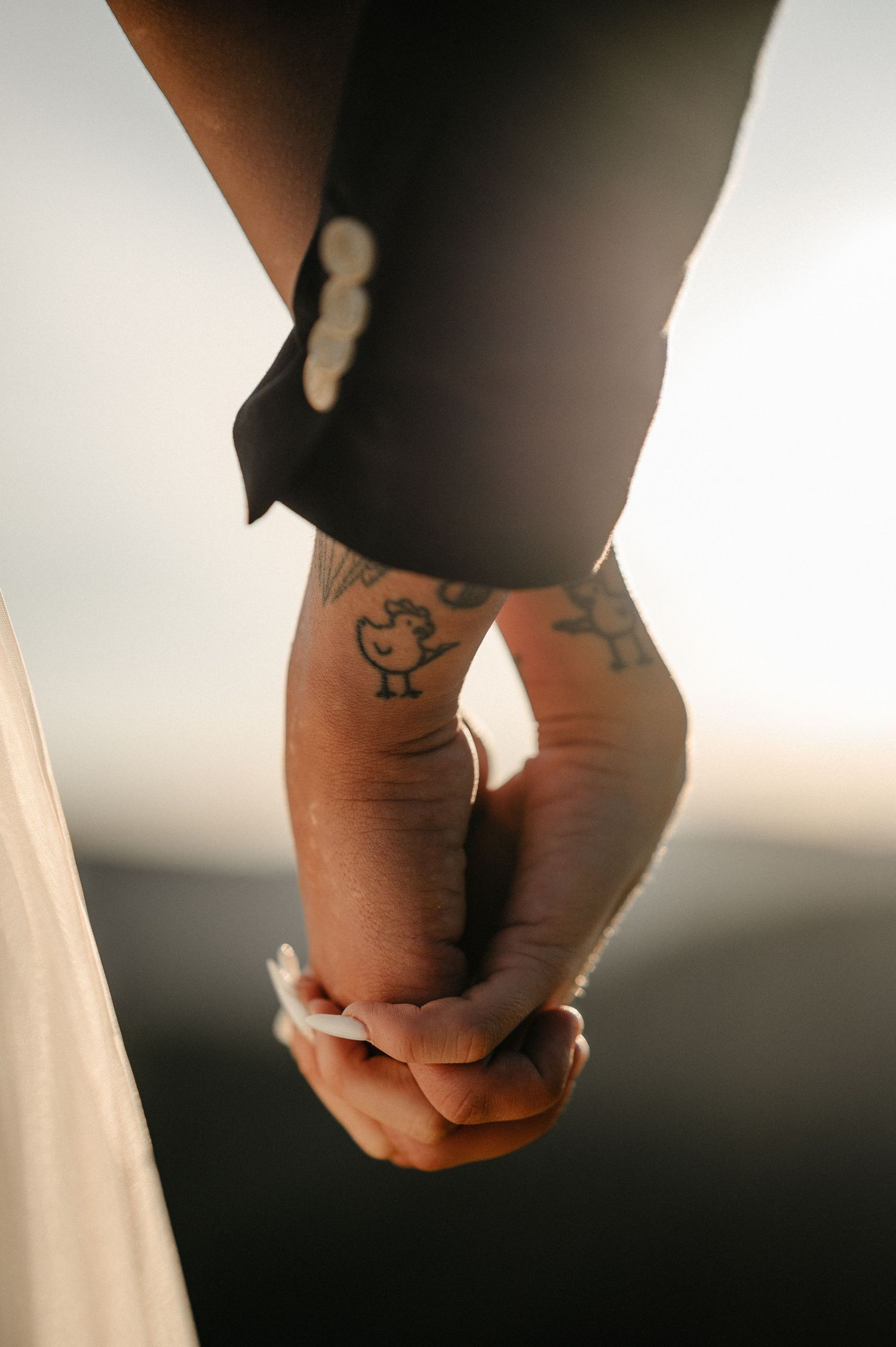 Close-up of bride and groom holding hands, groom with tattoos visible on wrist.