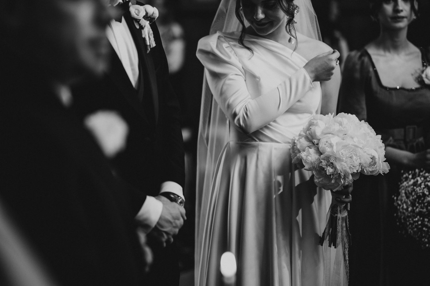 Black and white photo of bride in elegant gown holding white bouquet at wedding.