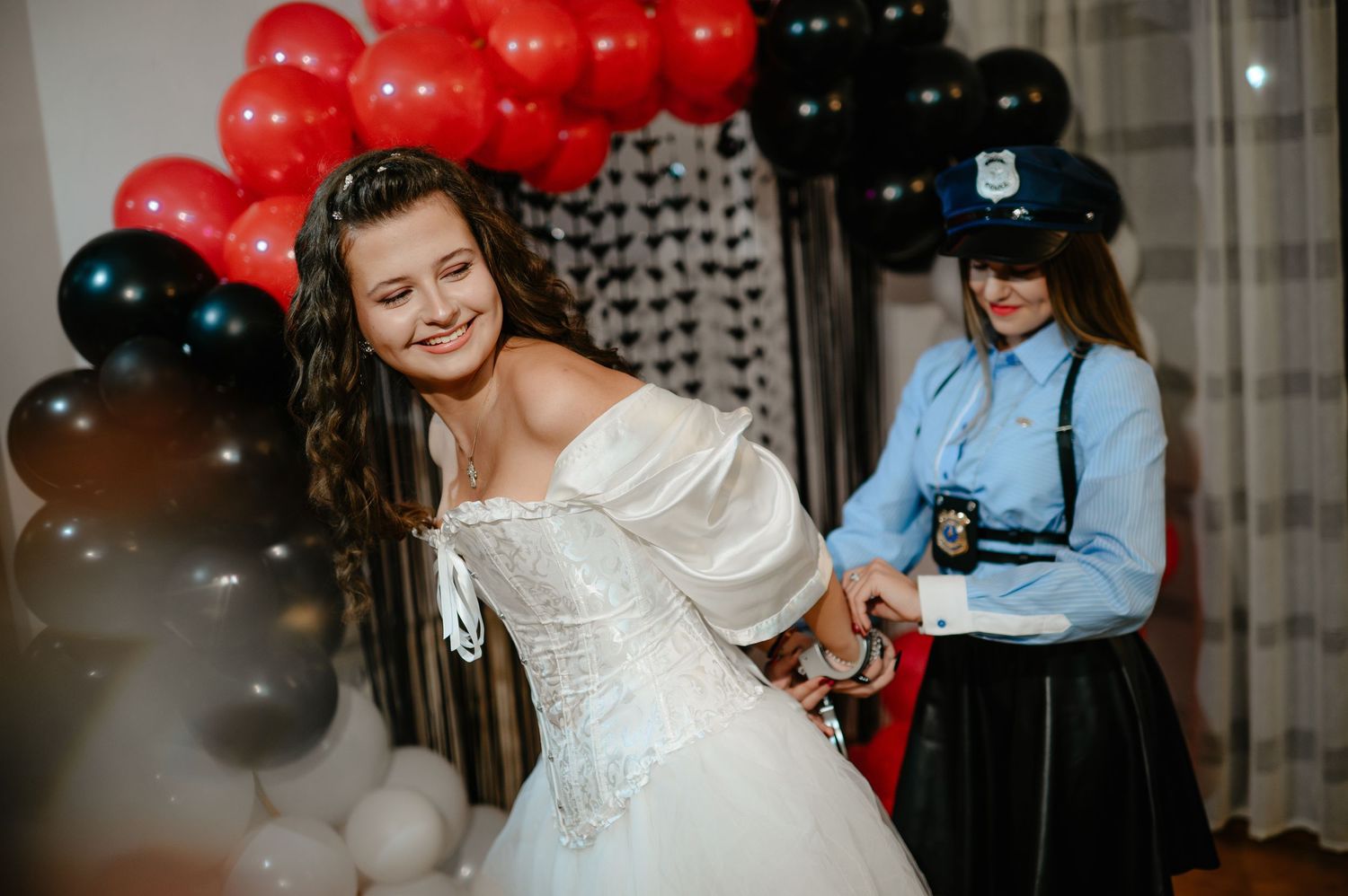 Woman in white bridal gown interacts with friend dressed as police officer at Halloween party.