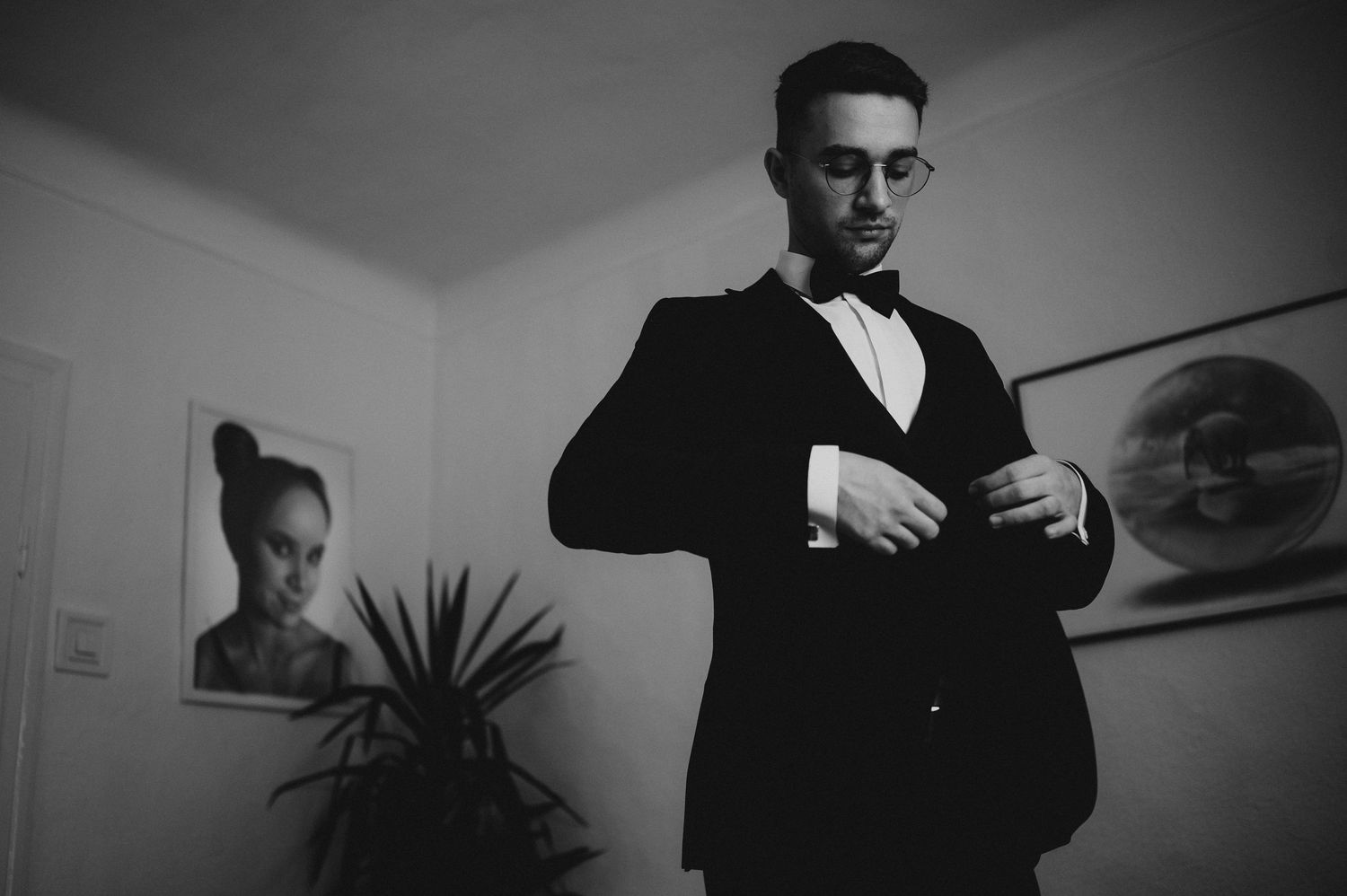 Man in tuxedo and bow tie adjusting cufflinks in black and white wedding preparation photo.