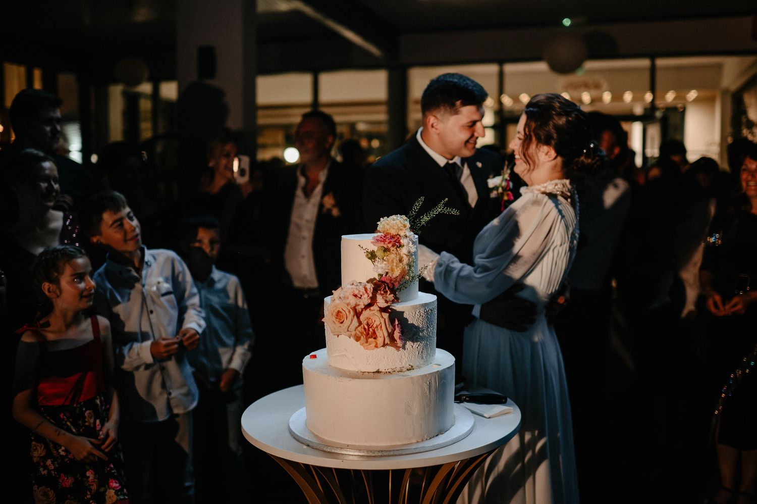 Bride and groom kissing while cutting floral wedding cake at reception.