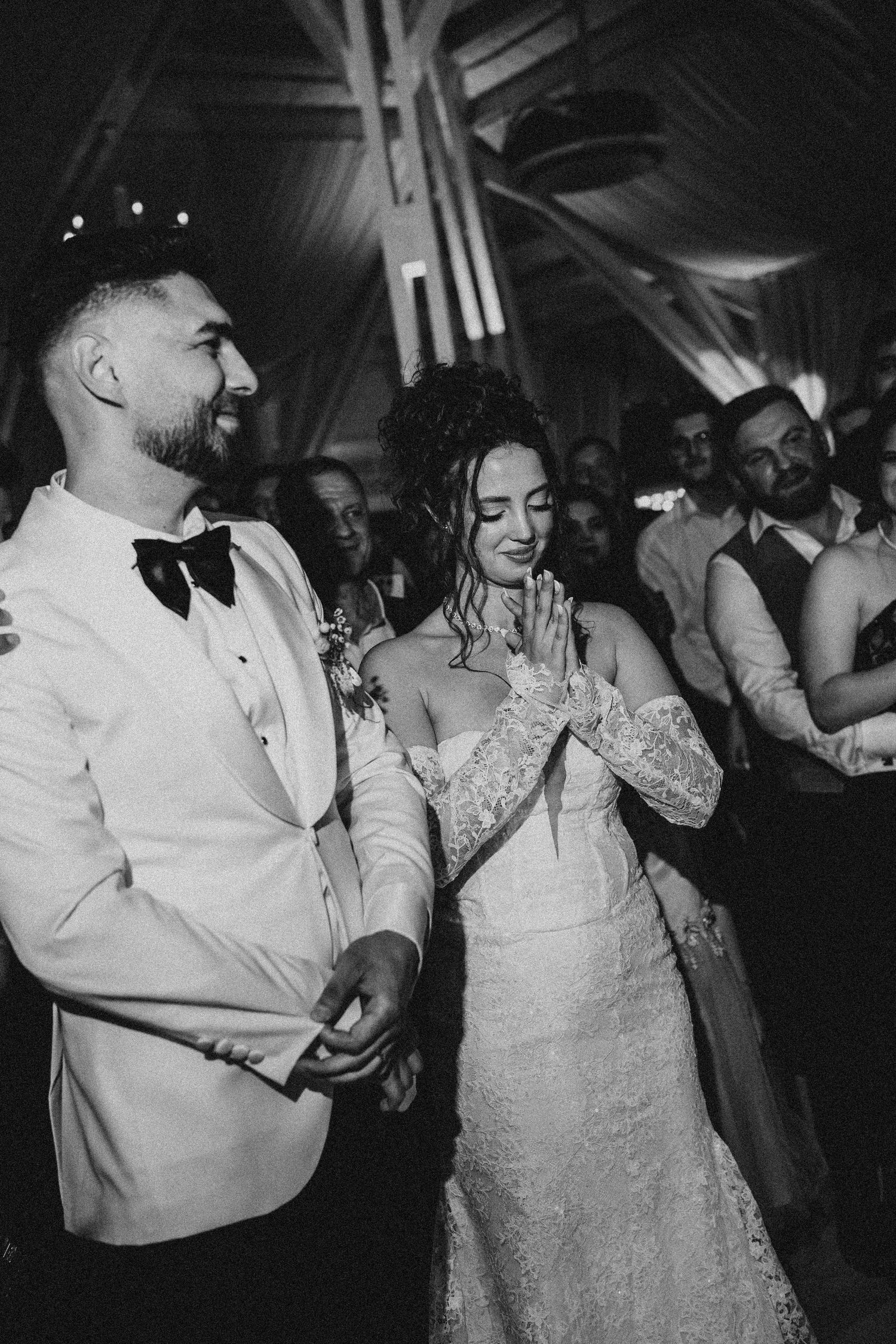 Black and white photo of a smiling bride and groom holding hands during their first dance at a wedding reception.