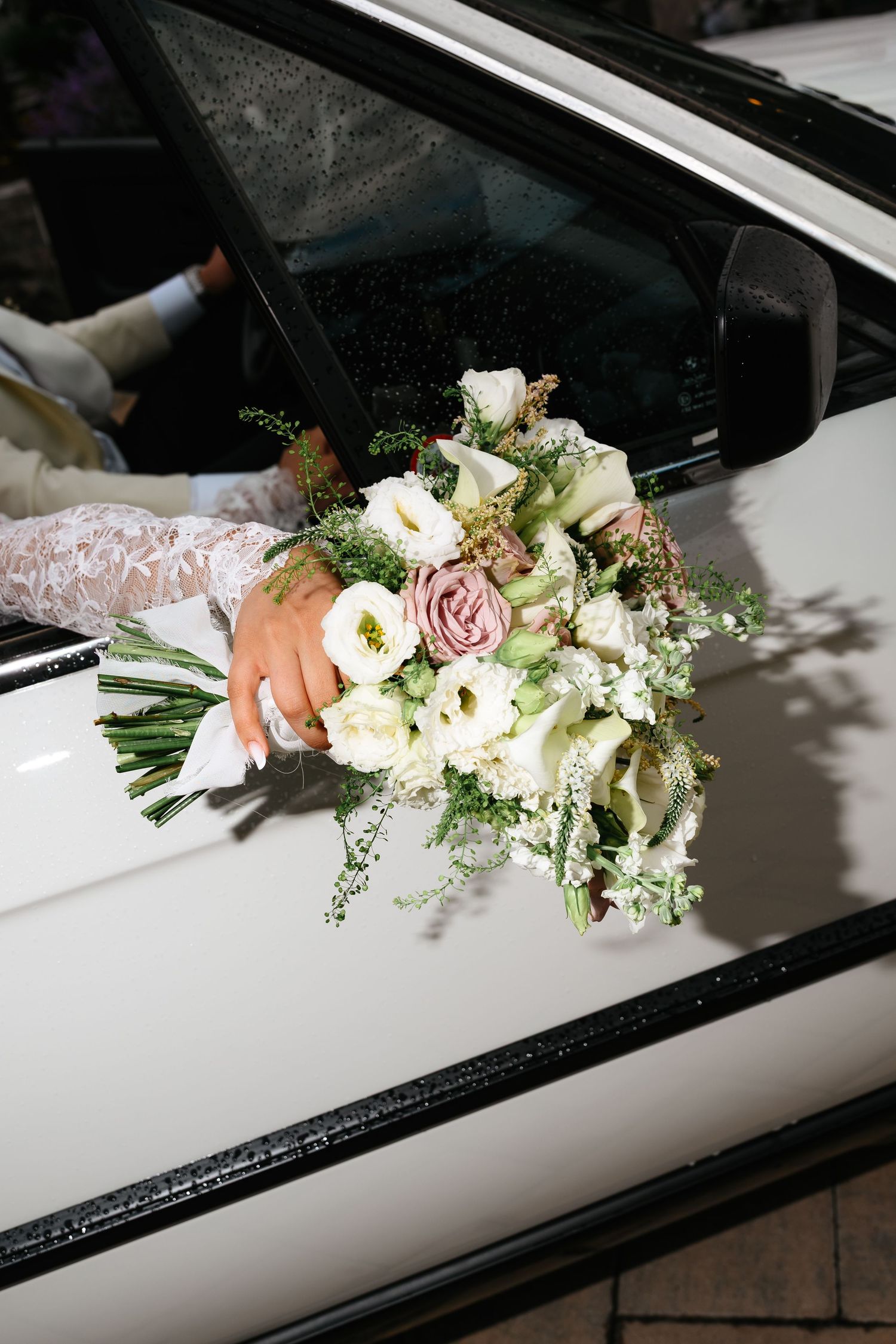 Bride holding a elegant wedding bouquet of white and pink roses out of a white car window.