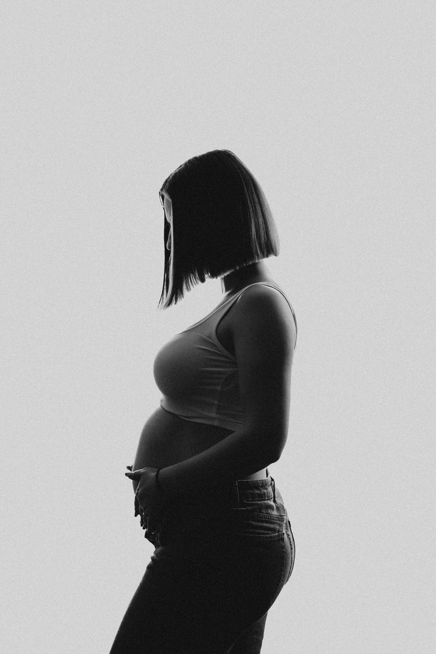 Black and white silhouette of a pregnant woman in profile, wearing a tank top and jeans.