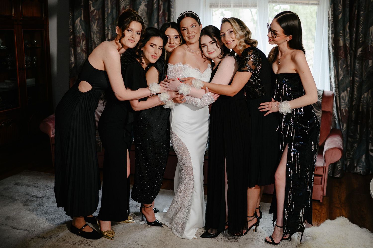 Bride in fitted white gown poses with six bridesmaids in black dresses holding bouquet.