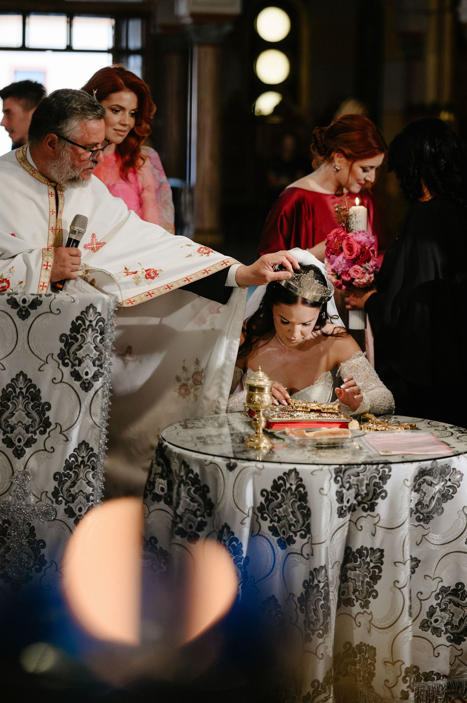 Orthodox priest crowning bride at altar during traditional church wedding ceremony with candles.