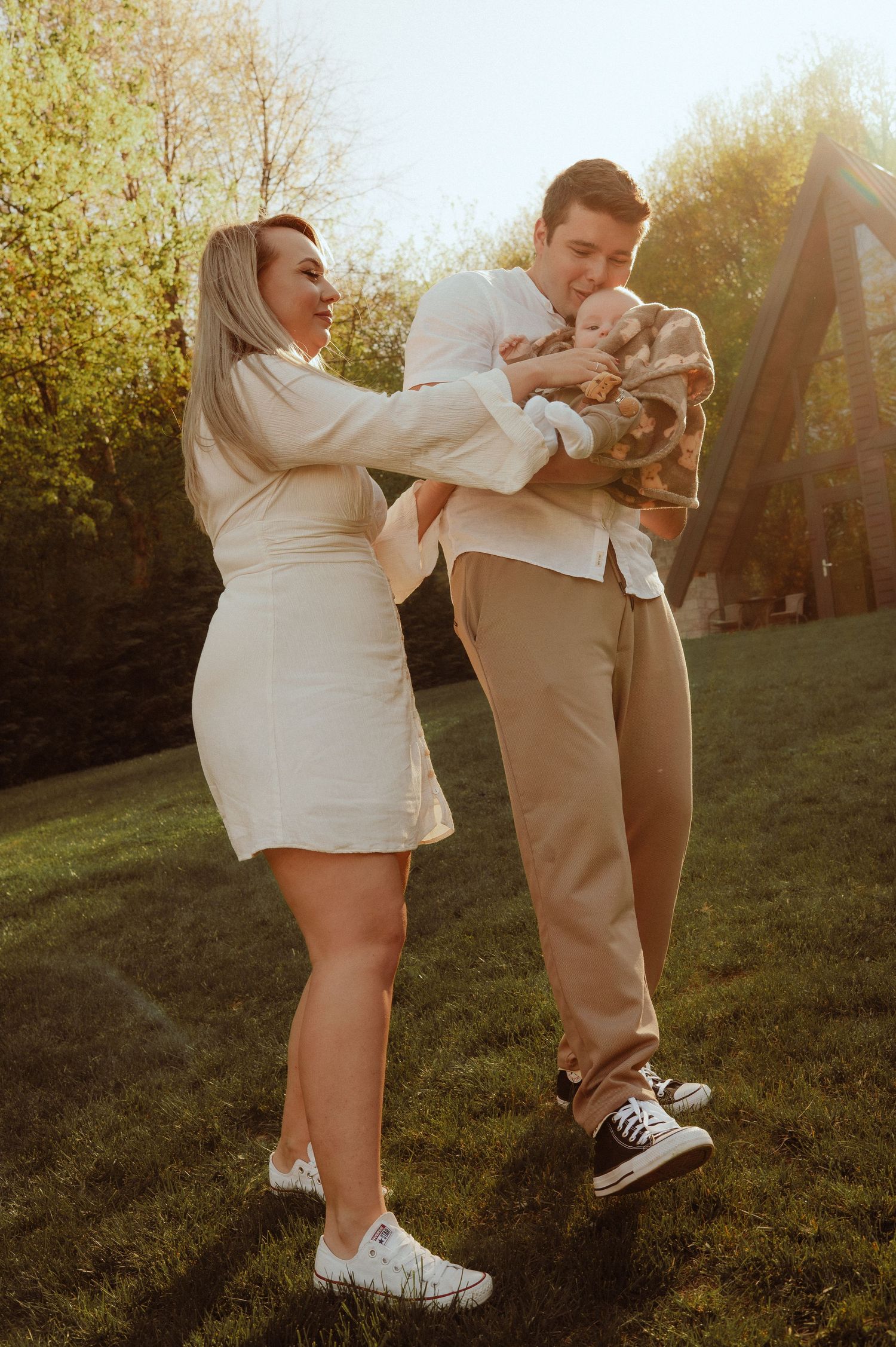 Happy young family with newborn baby sharing a joyful moment outdoors in warm golden sunset light.