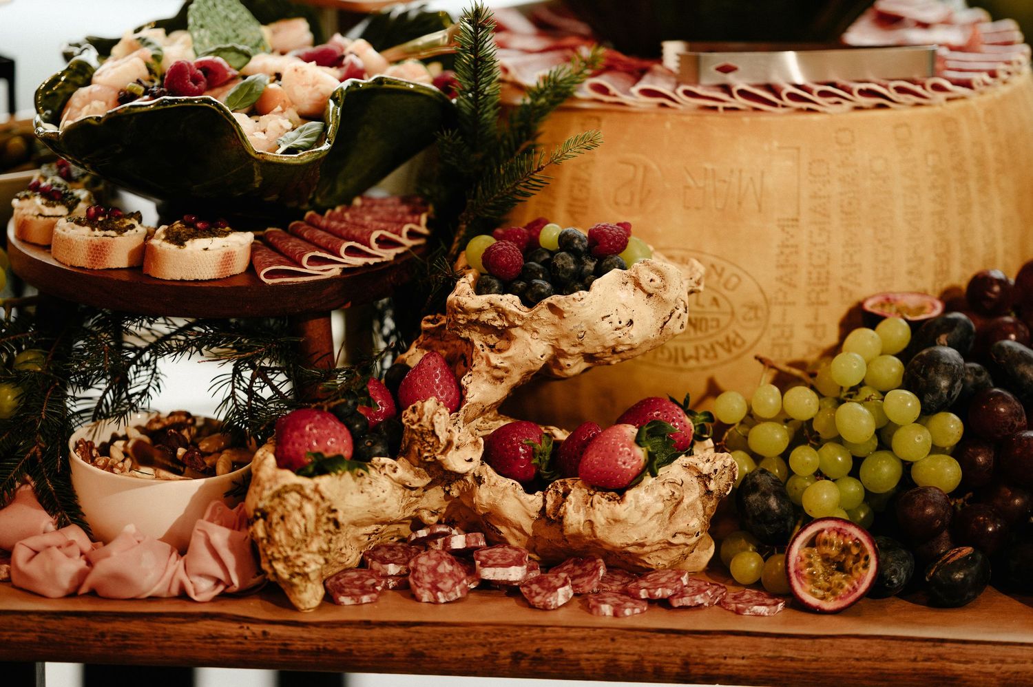 Upscale charcuterie display with aged cheese wheel, strawberries, grapes, salami roses, and gourmet accompaniments.