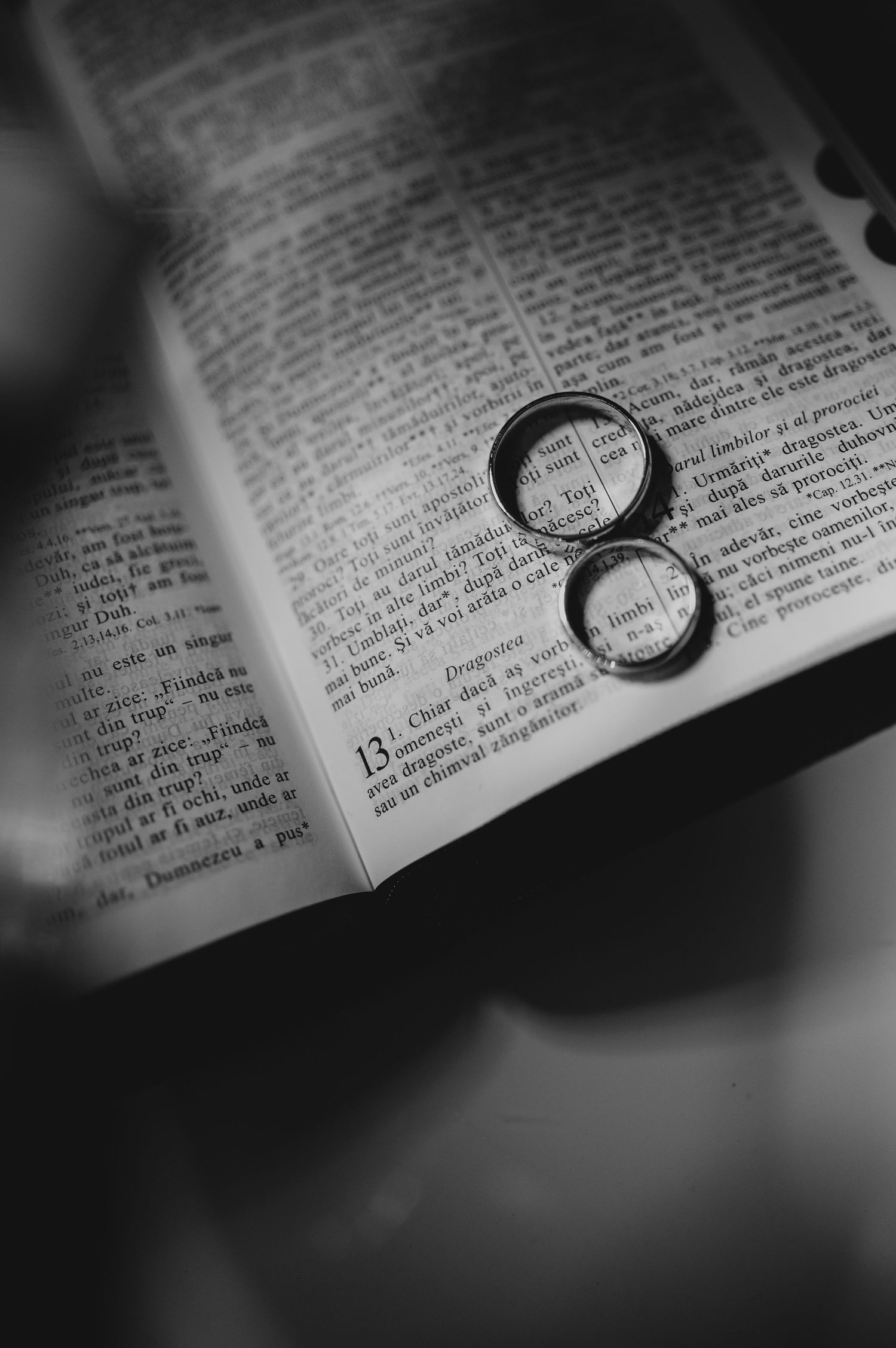 Two wedding rings resting on an open Bible page in black and white.
