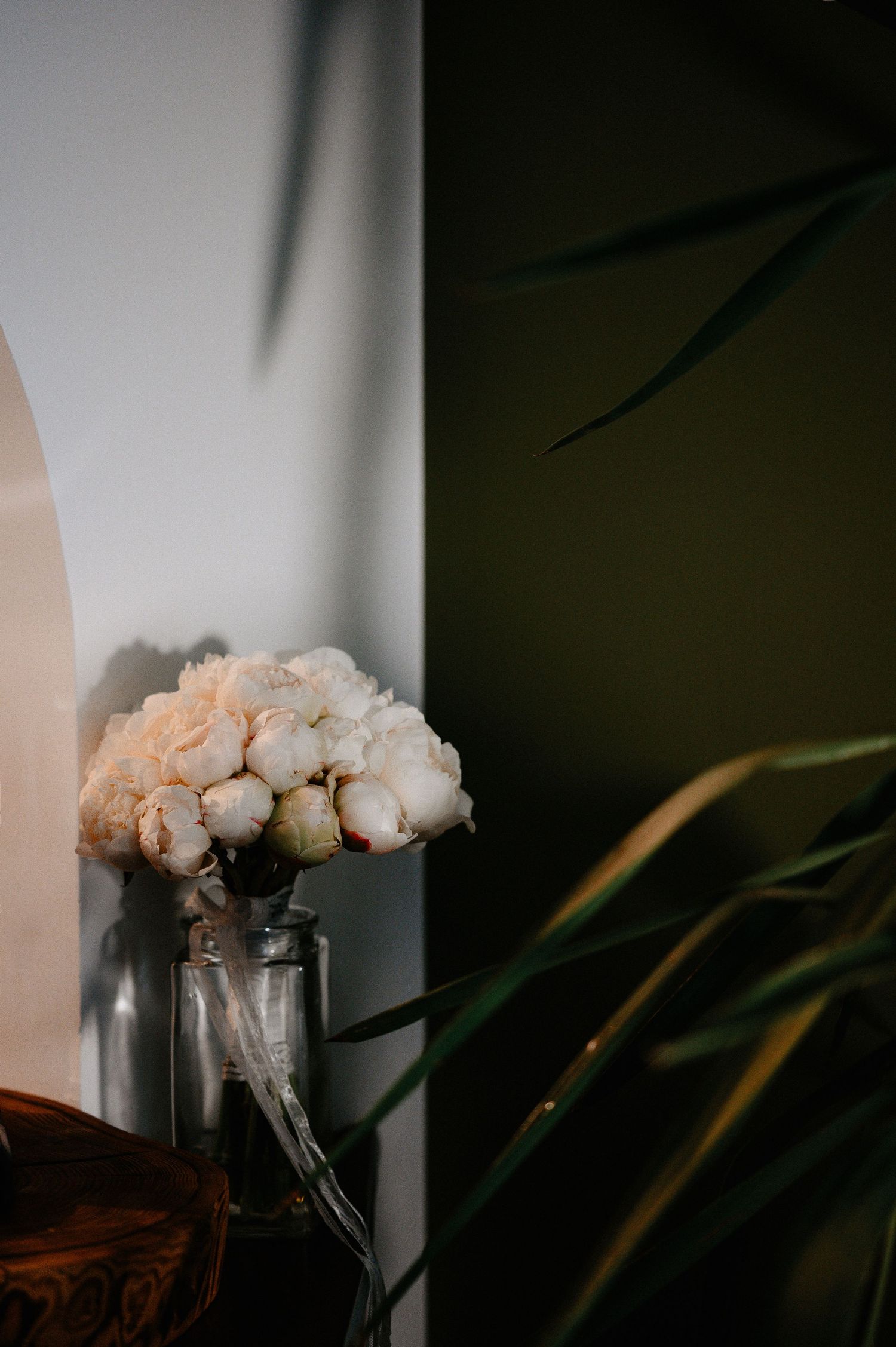Elegant white peony bridal bouquet in a glass vase against a white and dark green wall.