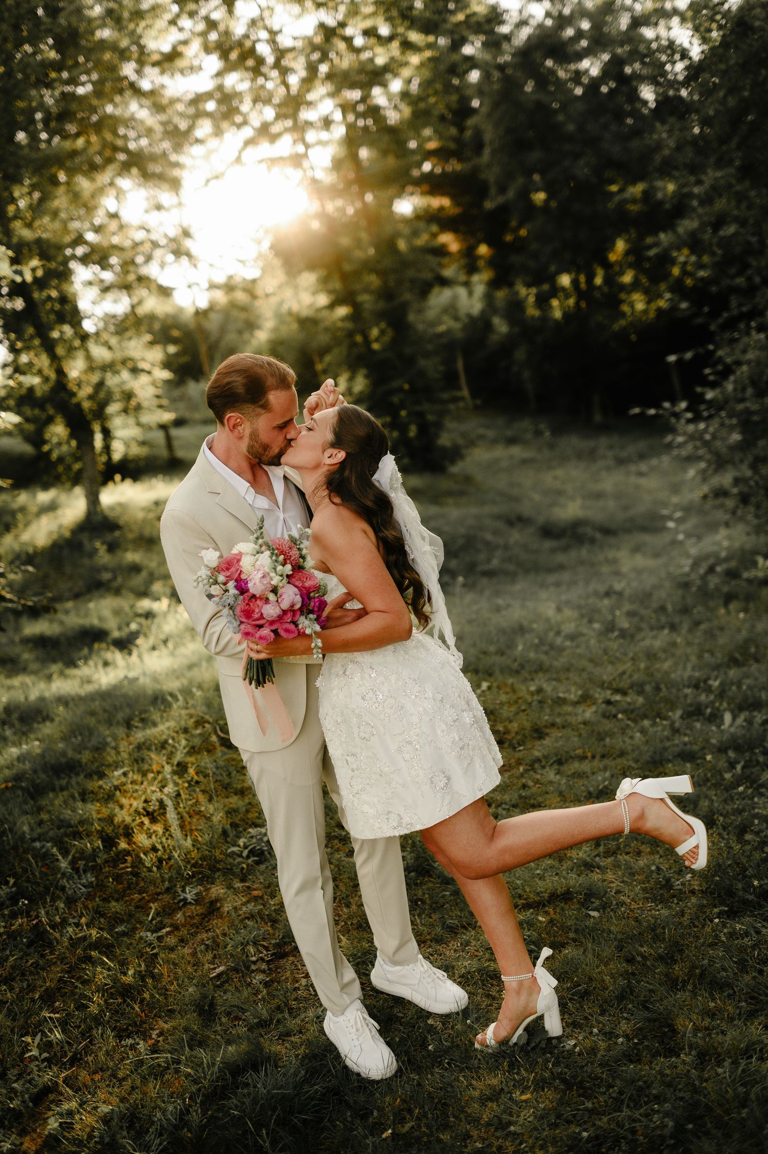 Bride and groom share a romantic kiss at golden hour in a lush green garden on their wedding day.