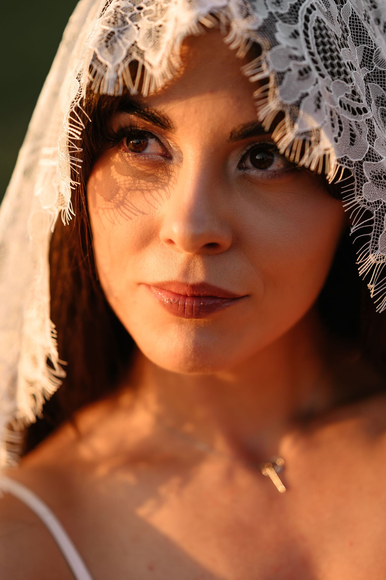Close-up portrait of a bride wearing a delicate white lace veil, bathed in warm golden hour sunlight.