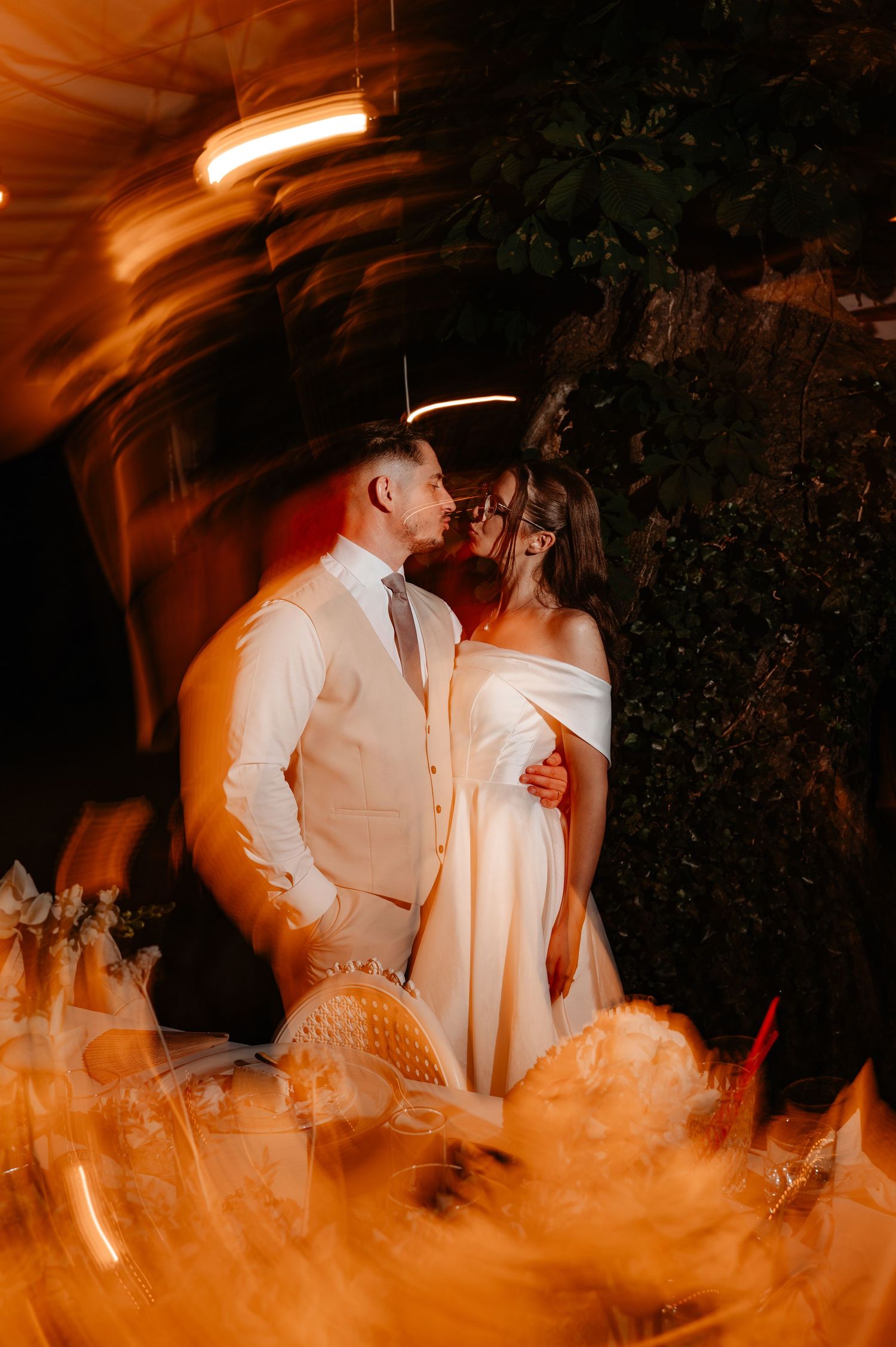 Bride and groom sharing an intimate moment surrounded by warm swirling light effects at outdoor night reception.