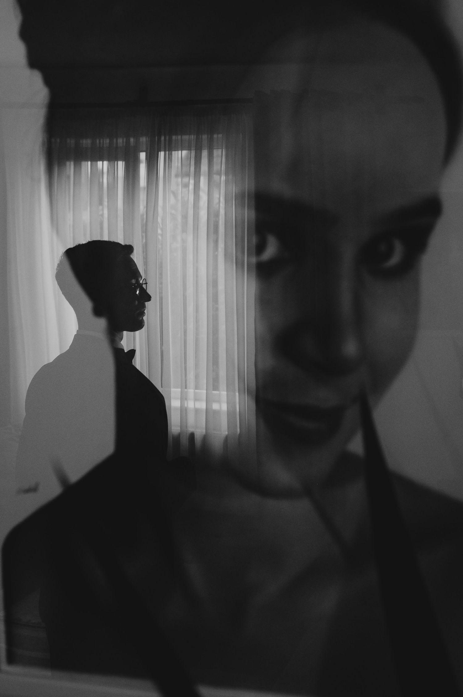 Black and white artistic mirror reflection portrait of a woman with dramatic shadows and silhouette in background.