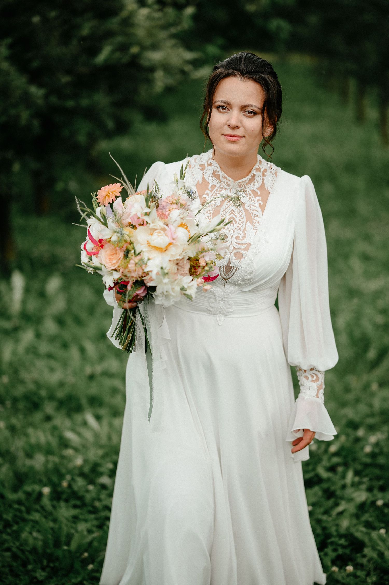Bride in vintage white lace gown holds peach and white bouquet in garden.
