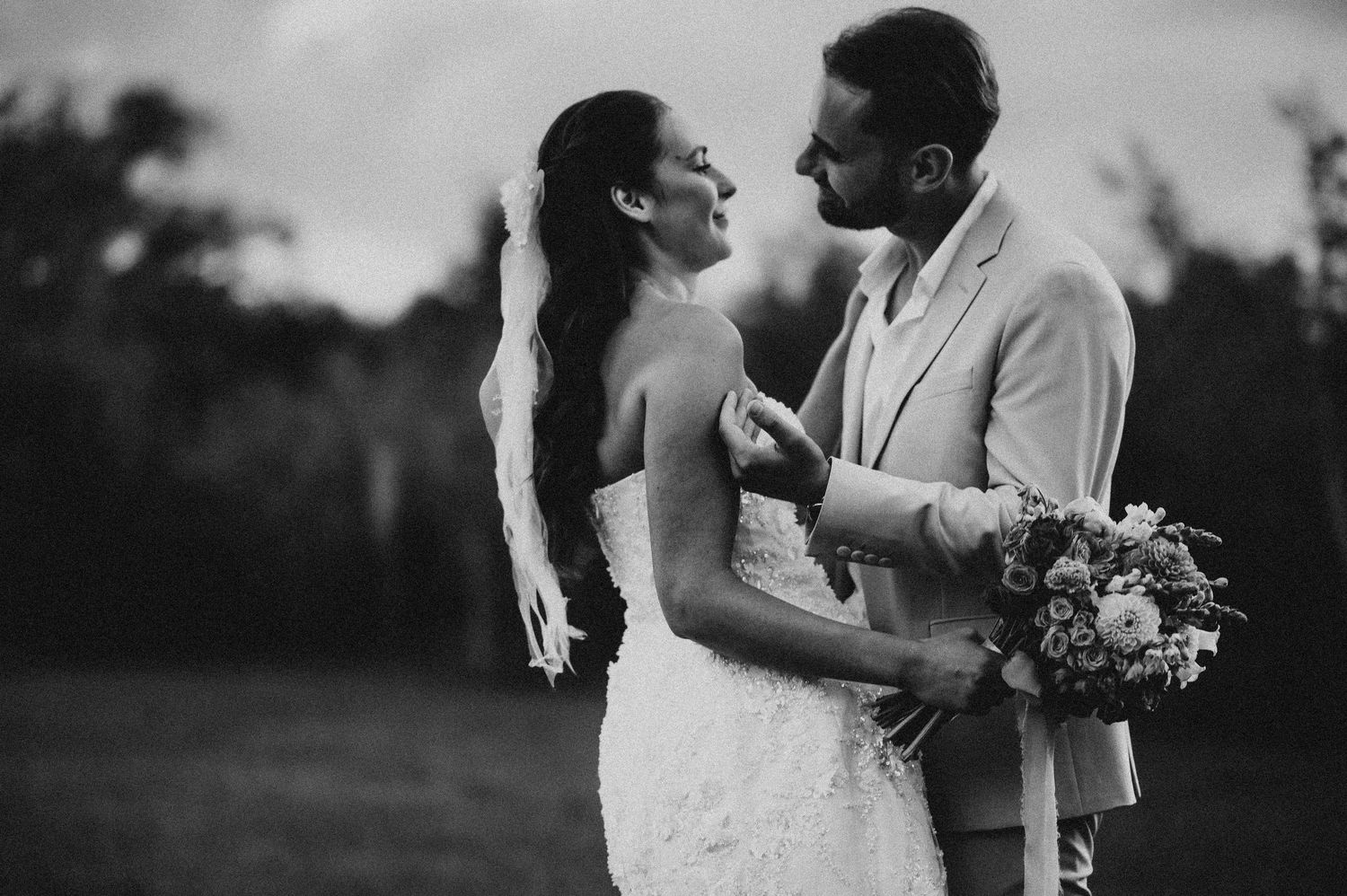 Black and white romantic portrait of bride and groom gazing at each other outdoors.