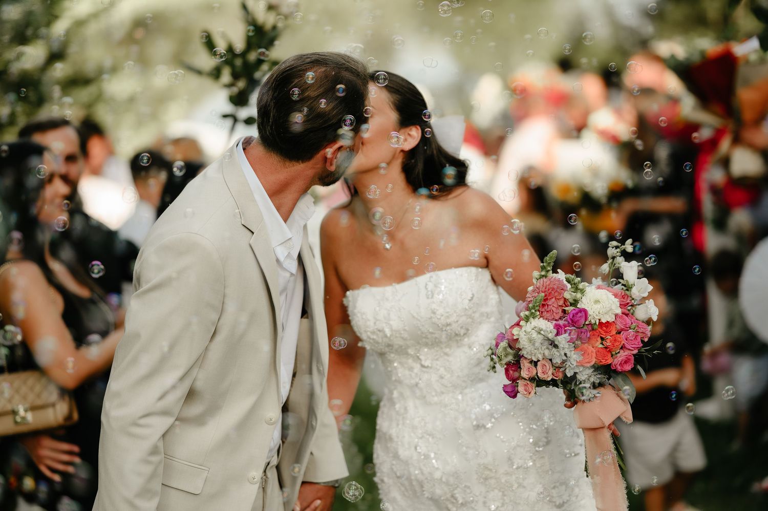 Bride and groom share a kiss surrounded by bubbles during their outdoor wedding ceremony.