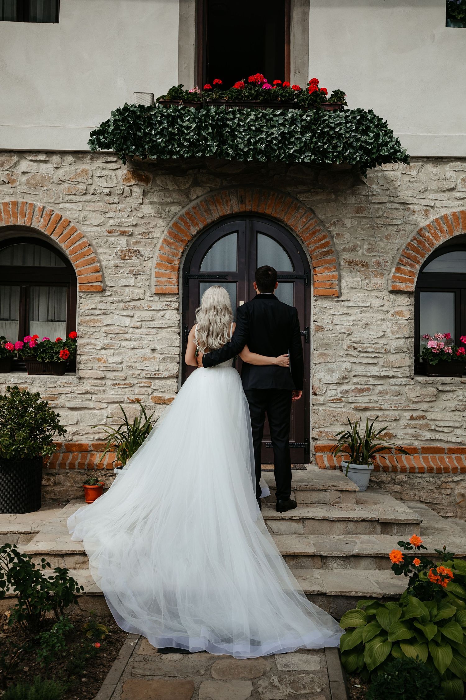 Bride and groom walking toward stone building entrance with lush floral decor.