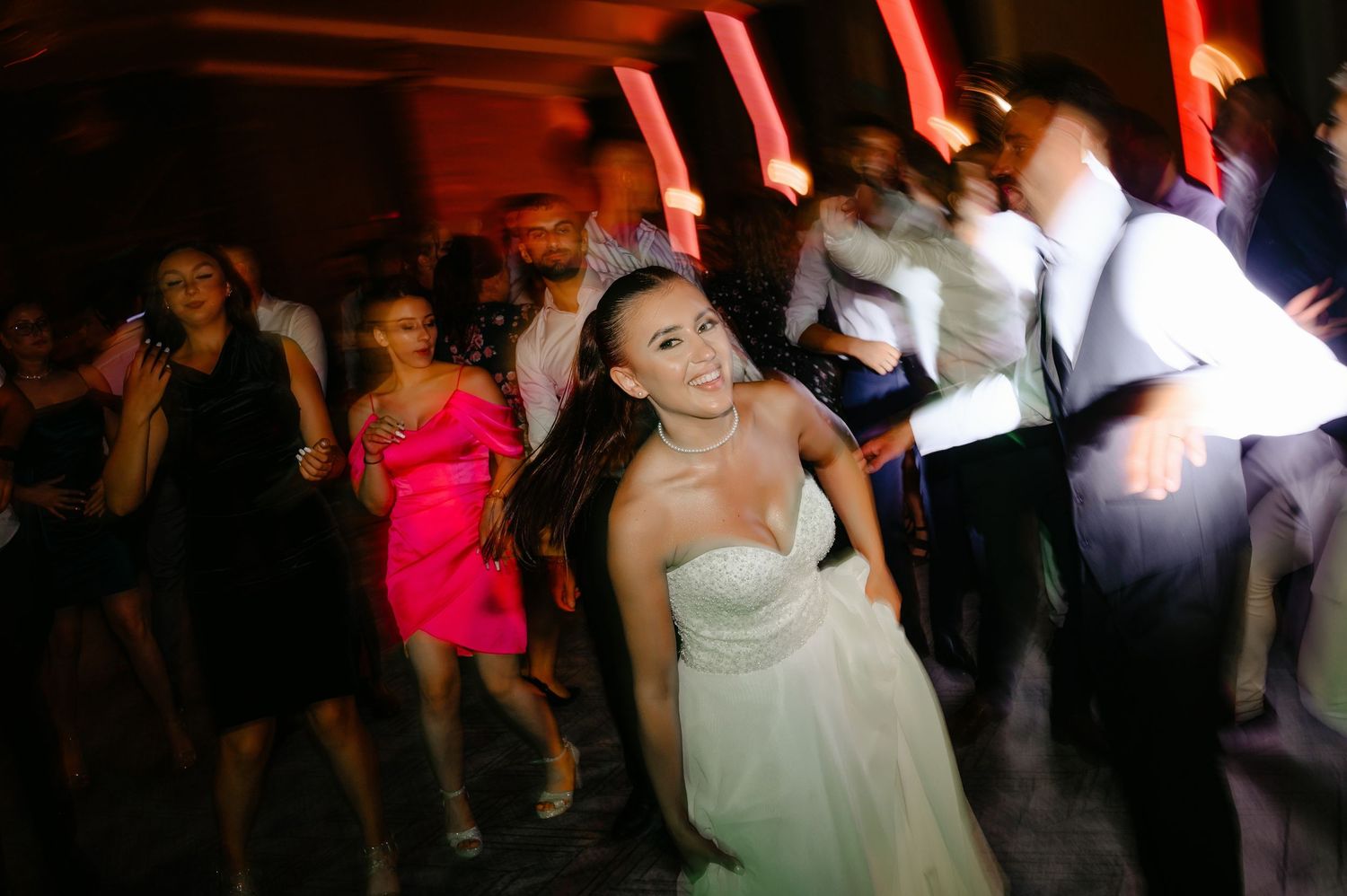 Bride in a strapless white gown dancing joyfully with guests at a lively wedding reception party.