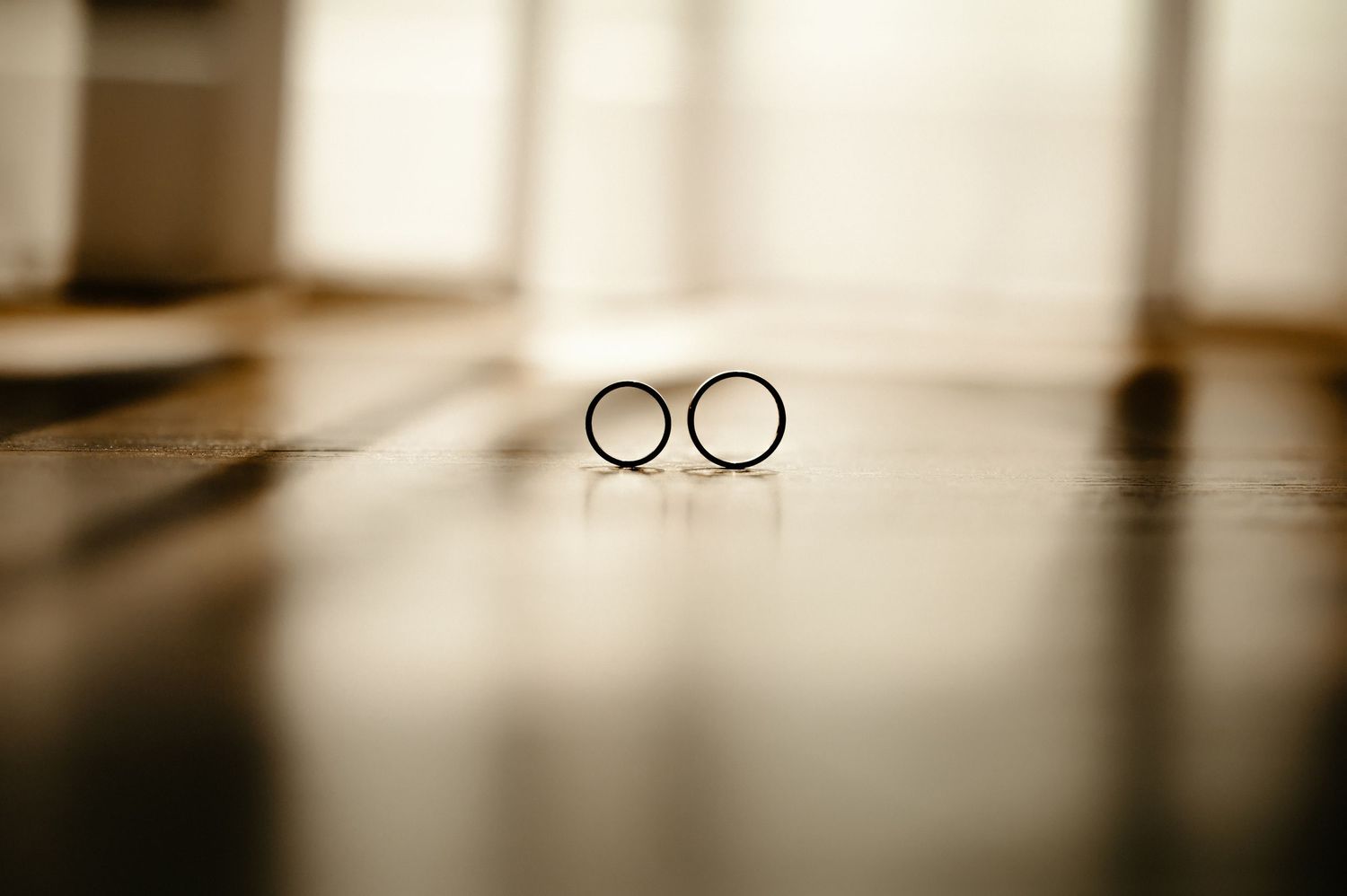 Two gold wedding bands standing upright side by side on a reflective wooden floor surface.
