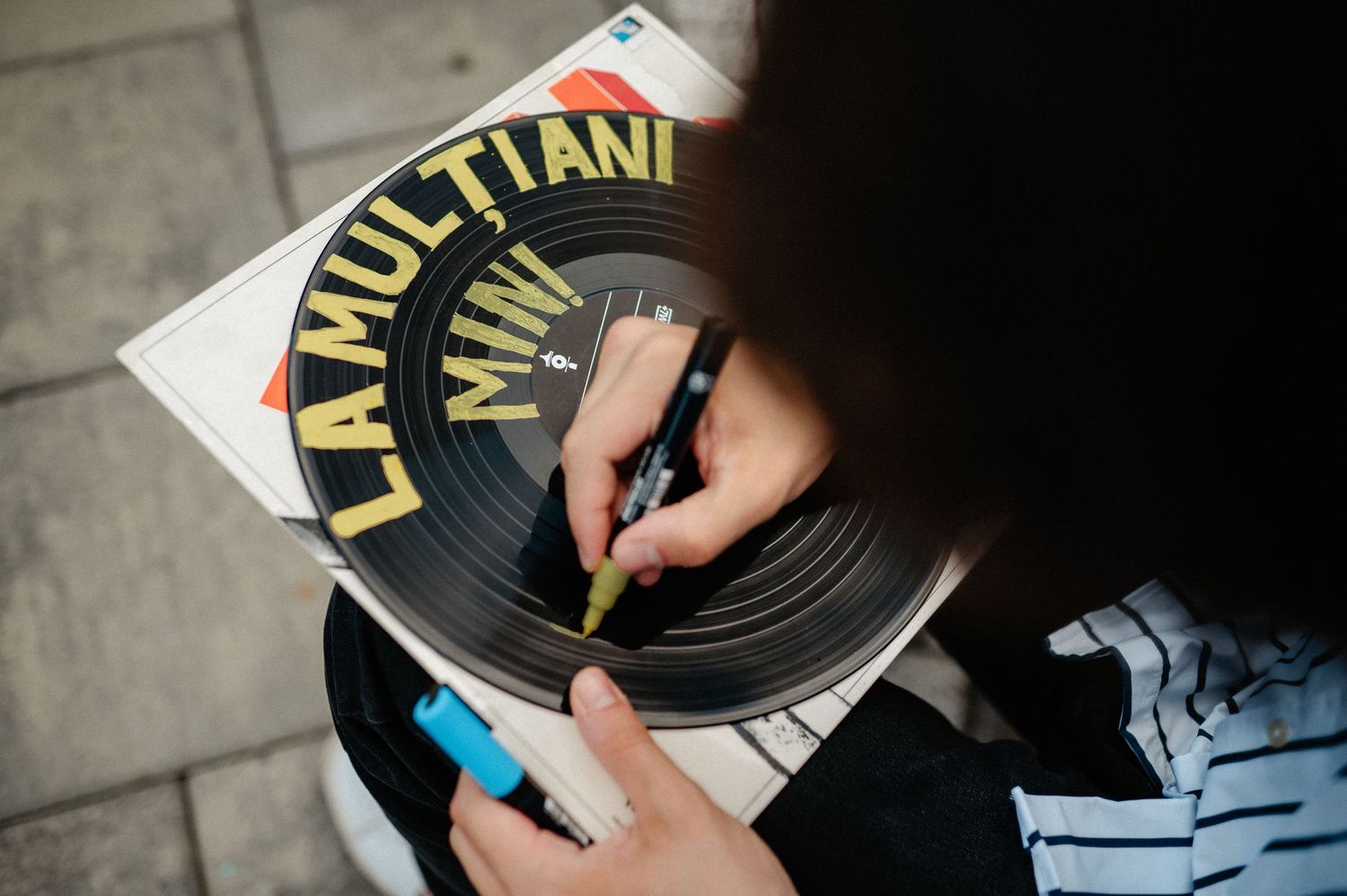 Person writing a birthday message on a vinyl record with gold lettering reading La Multi Ani.