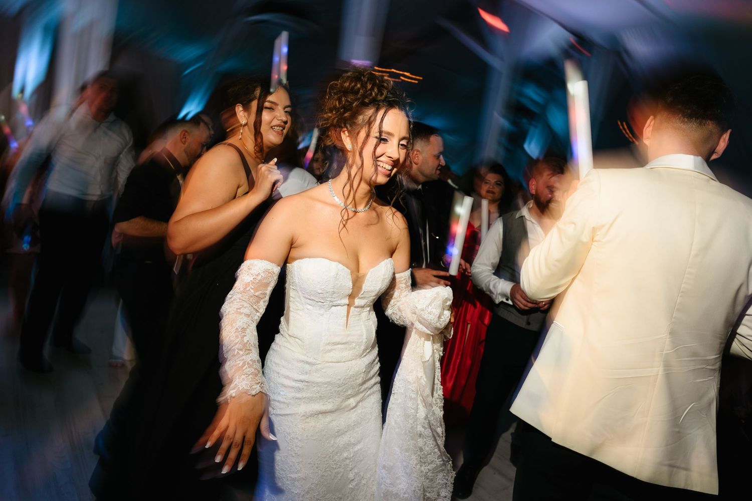 Bride in white lace gown dancing joyfully with guests at a lively wedding reception.